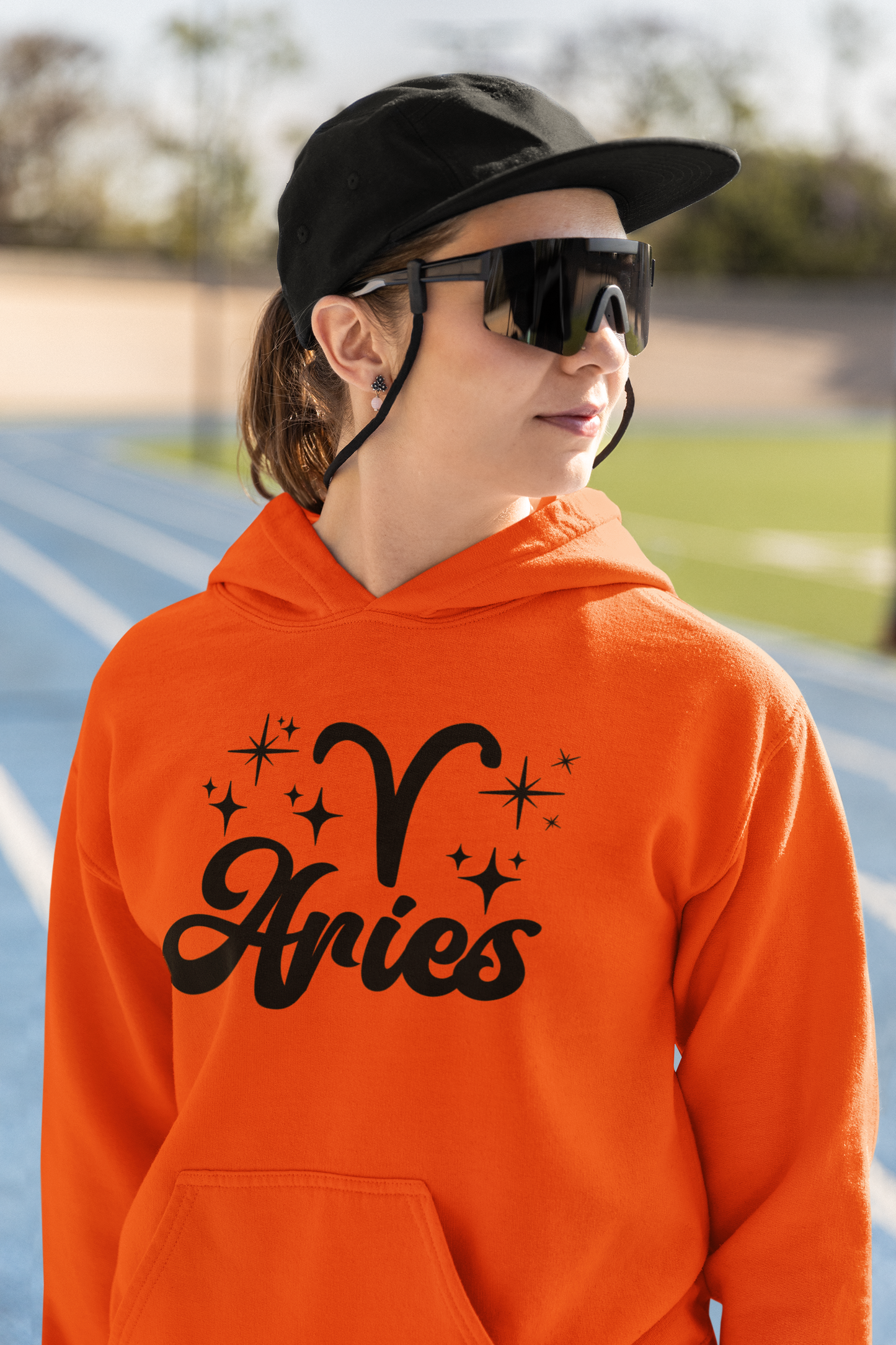 Person wearing a orange hoodie with black 'Aries' text and zodiac symbol outdoors.