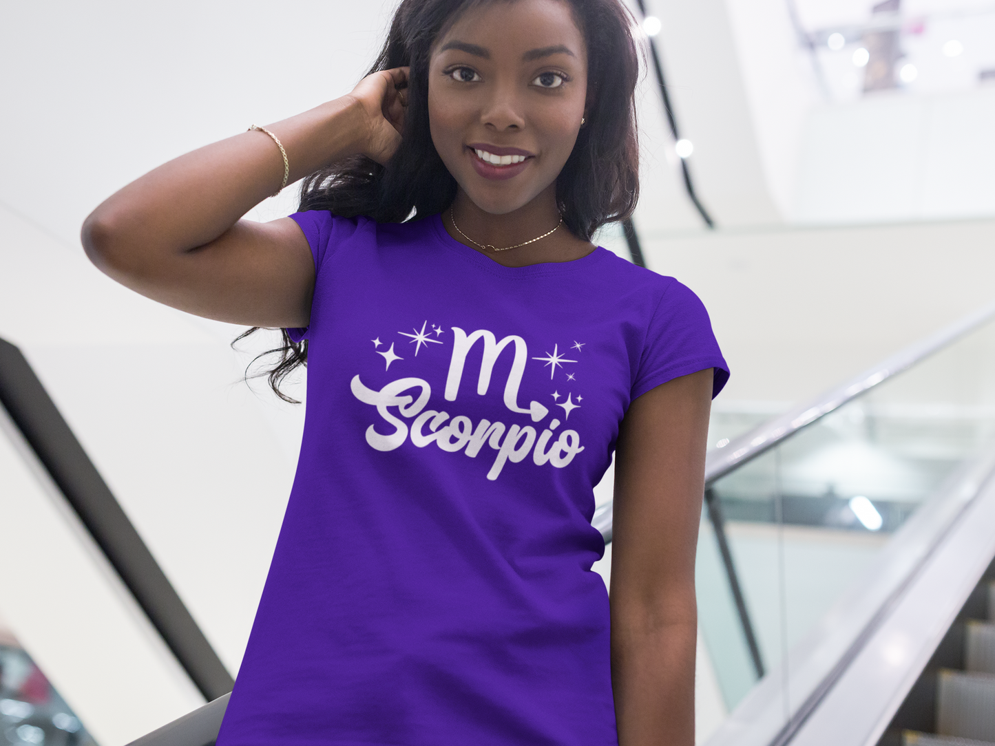 Woman wearing a purple t-shirt with 'Scorpio' white text design, standing on escalator.