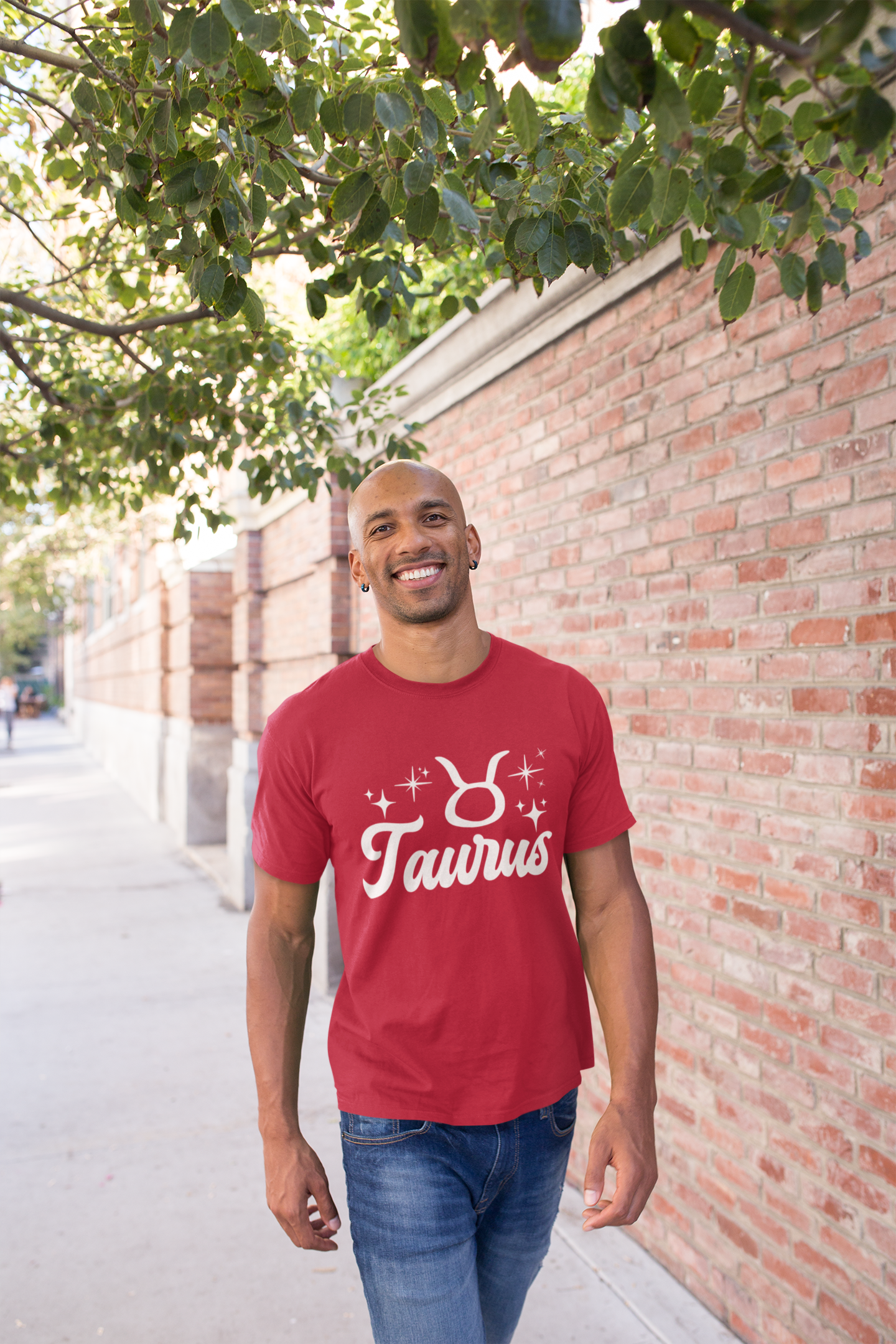 Man wearing a red t-shirt with 'Taurus' white text design, walking outdoors near a brick wall and tree.