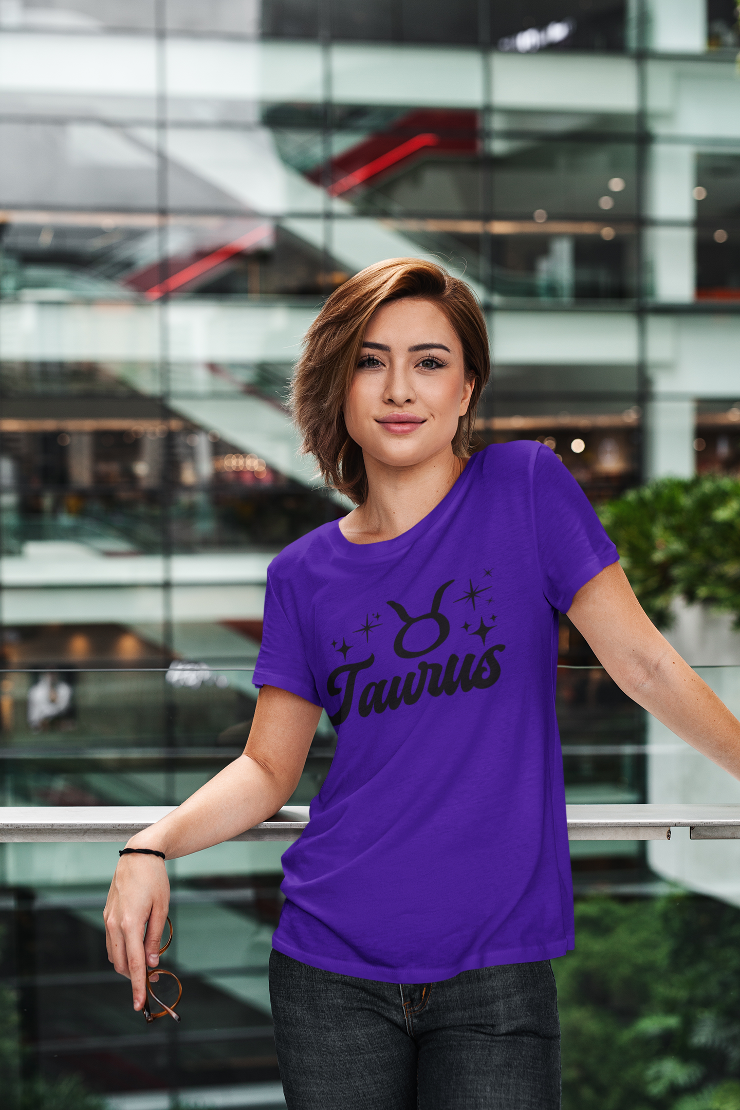 Person wearing a purple Taurus t-shirt, black text design in front of a modern building.