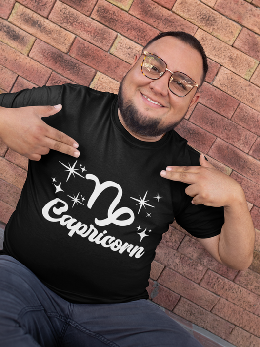 Man wearing a black t-shirt with 'Capricorn' white text design, pointing at it, against a brick wall.