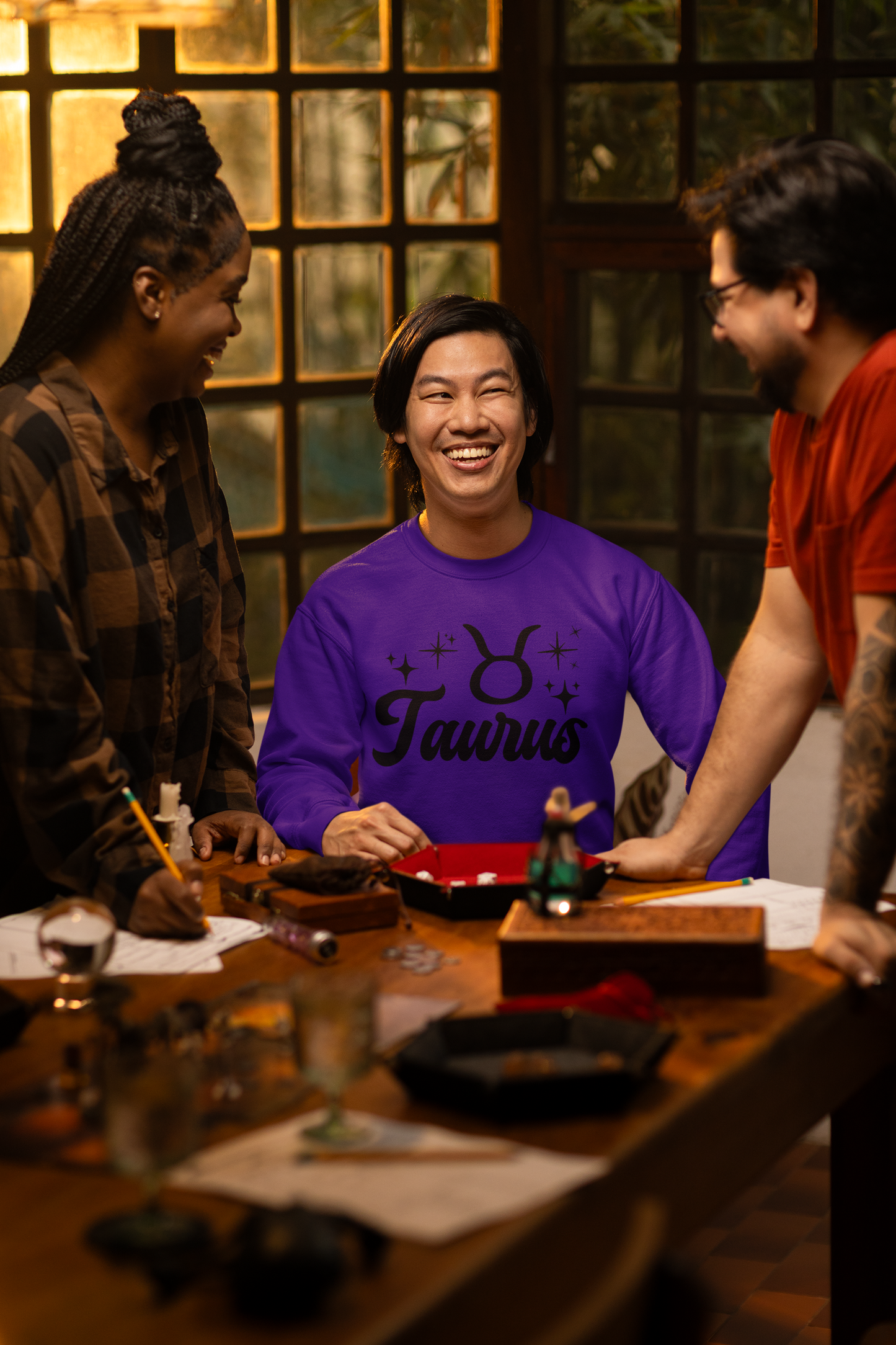 Three people around a table with a focus on a person wearing a purple 'Taurus' black text t-shirt.