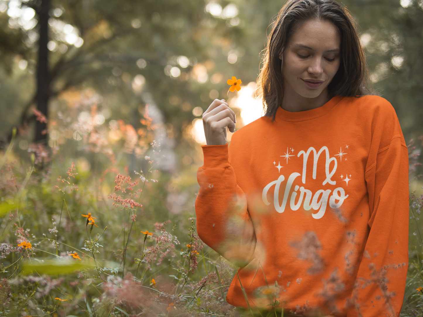 Woman wearing a orange 'Virgo' white text design sweatshirt in a field of flowers
