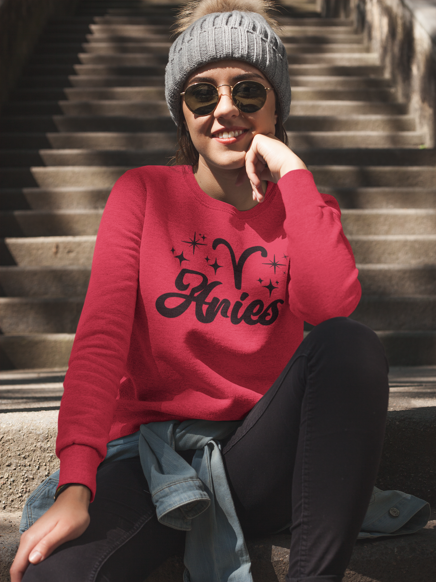 Person wearing a red 'Aries' black text design sweatshirt sitting on steps.