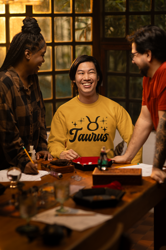 Three people around a table with a focus on a person wearing a gold 'Taurus' black text t-shirt.