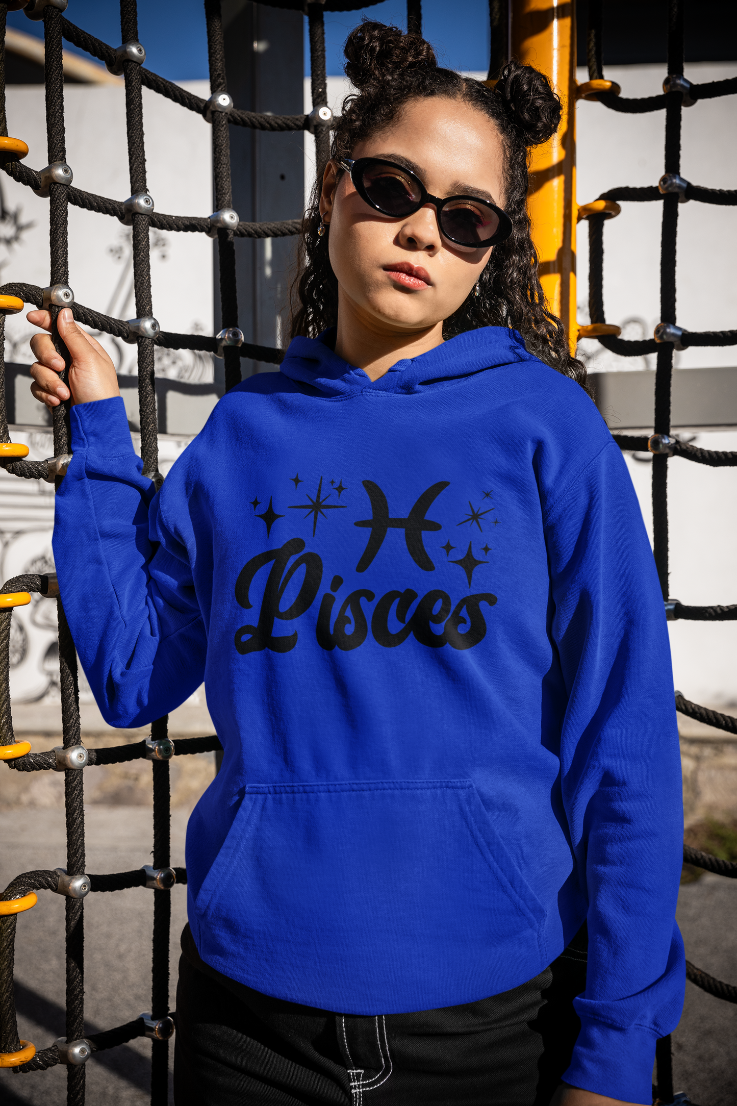 Person wearing a blue hoodie with 'Pisces' black text with zodiac symbol, standing in front of playground equipment.