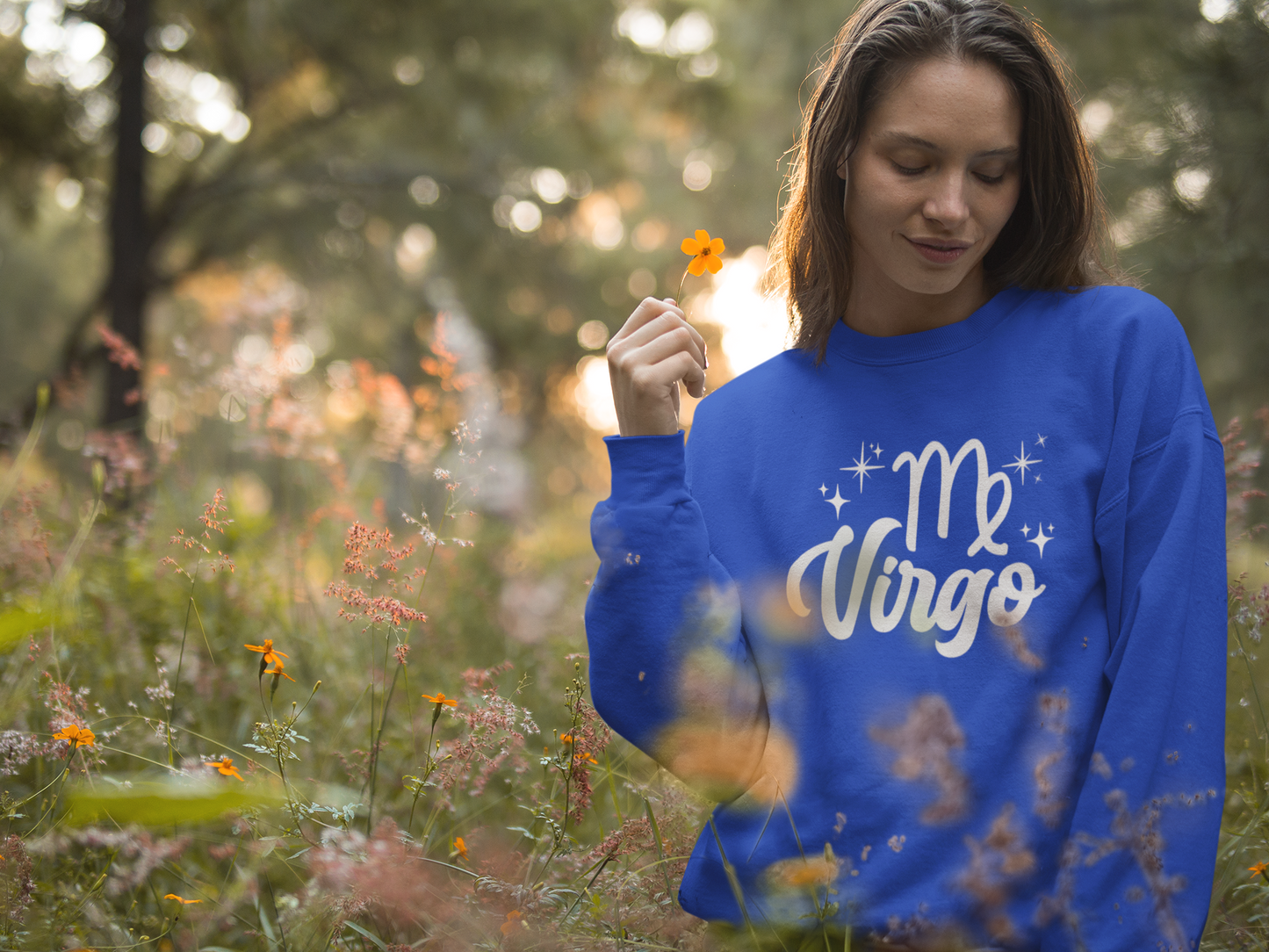 Woman wearing a blue 'Virgo' white text design sweatshirt in a field of flowers