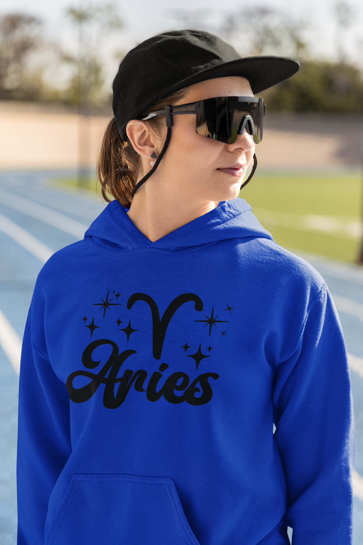 Person wearing a blue hoodie with black 'Aries' text and zodiac symbol outdoors.