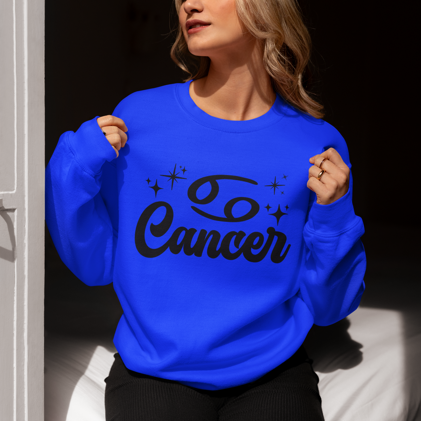 Person wearing a blue sweatshirt with 'Cancer' black text, sitting indoors.