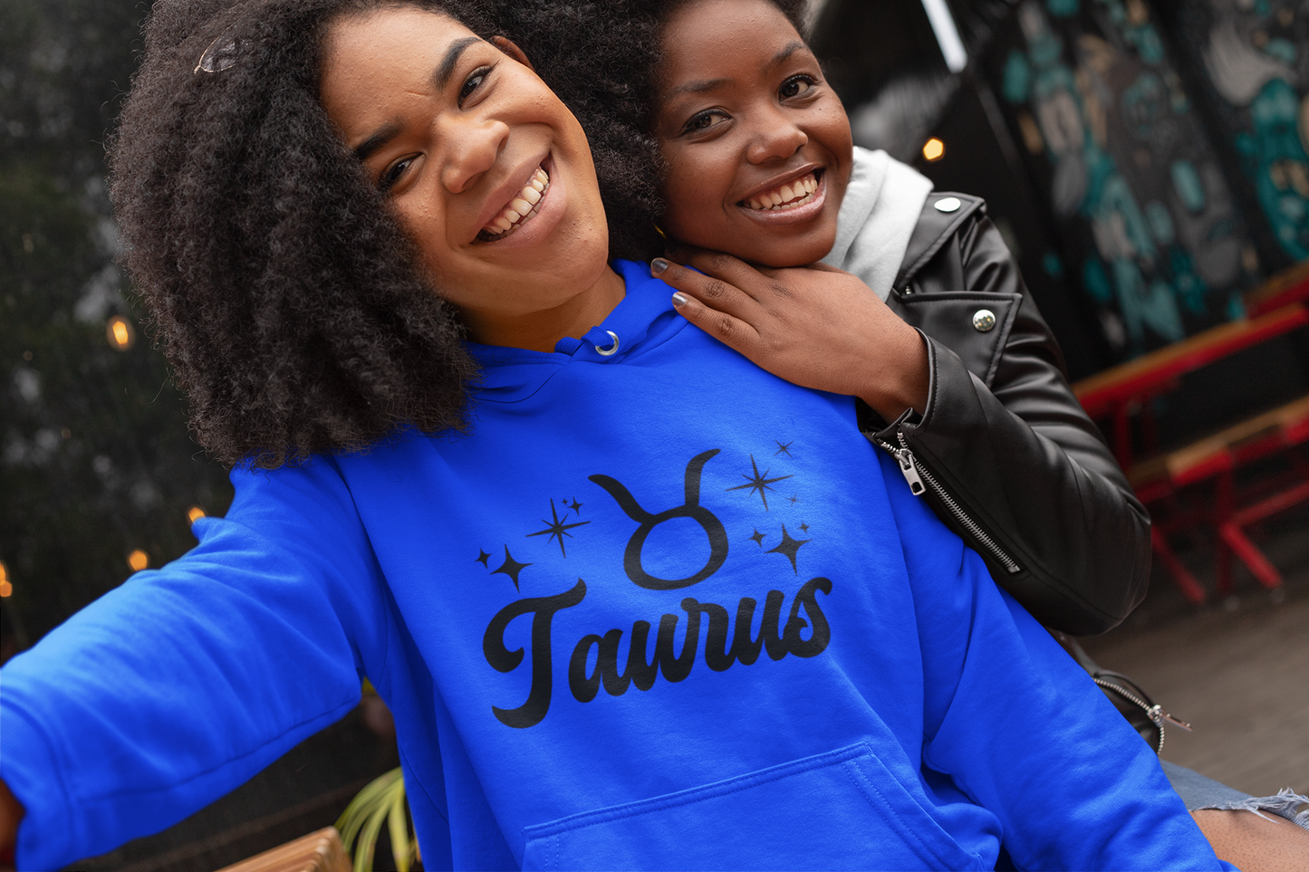 Two people posing together, one wearing a blue 'Taurus' hoodie, black text design 