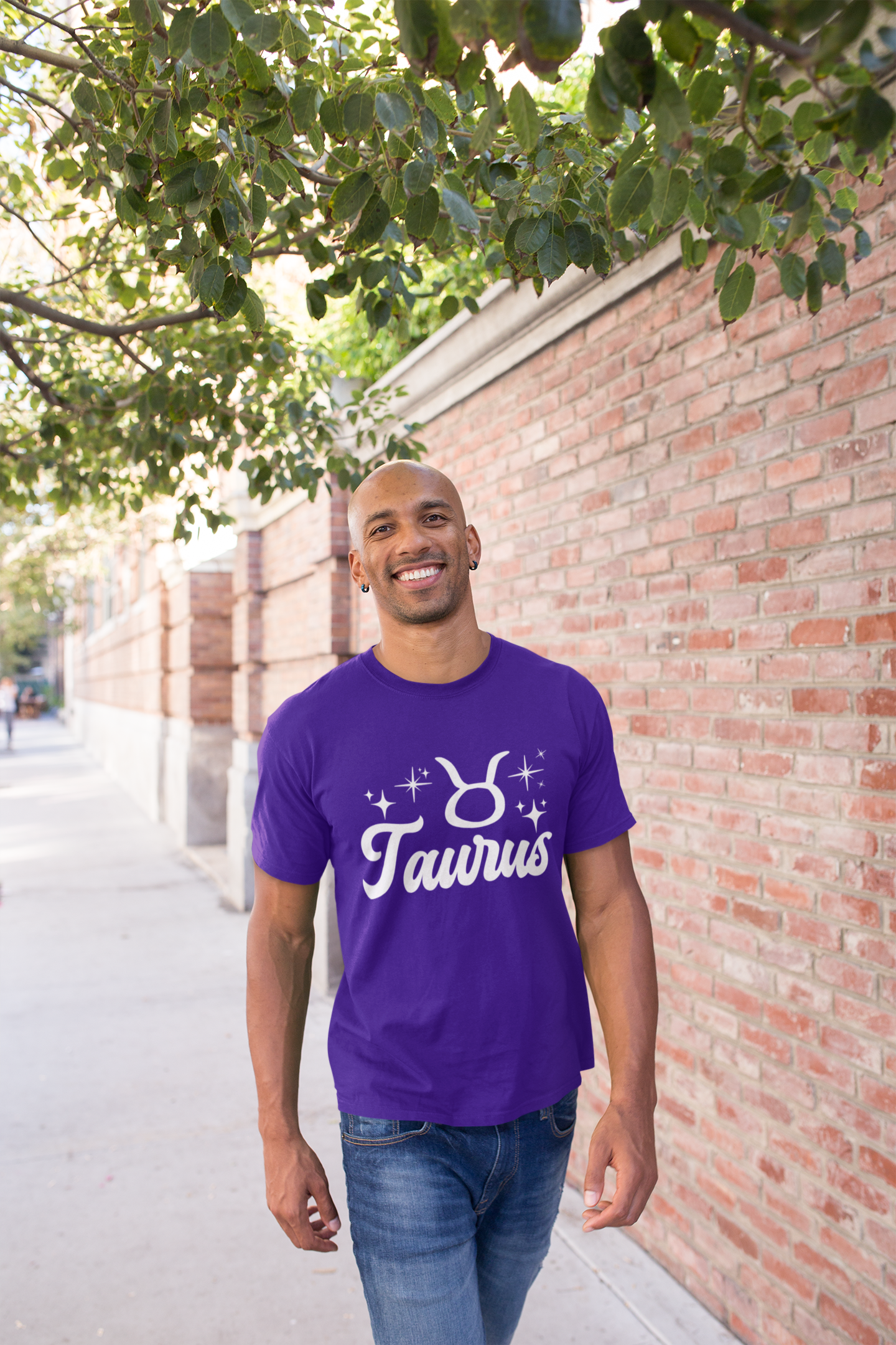 Man wearing a purple t-shirt with 'Taurus' white text design, walking outdoors near a brick wall and tree.