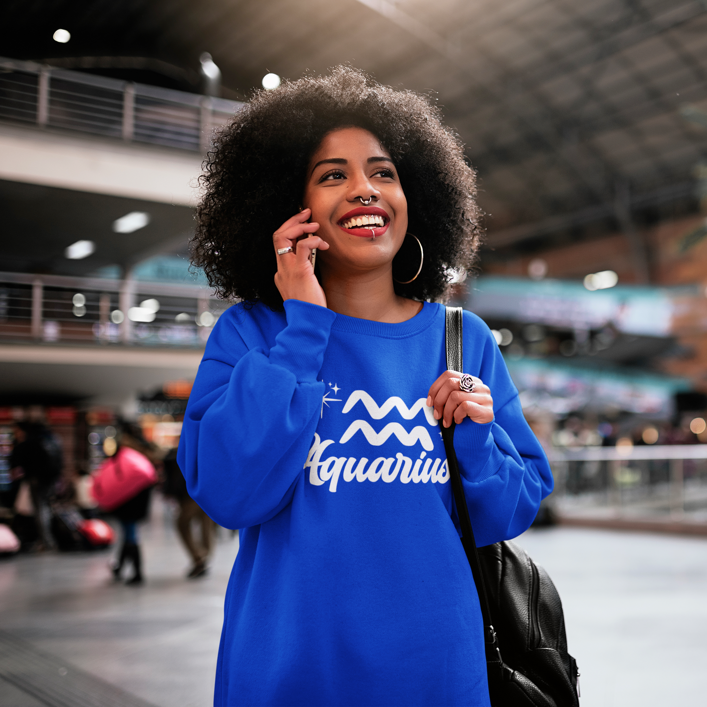 Woman in a blue 'Aquarius' white text design sweatshirt talking on a phone in an indoor setting