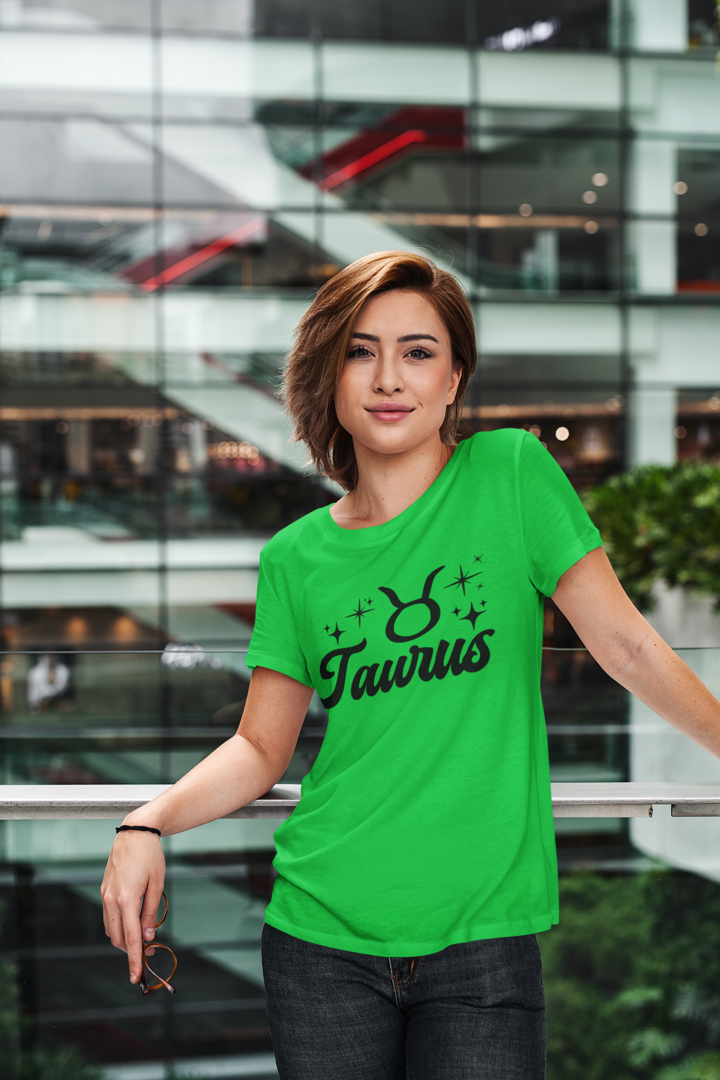 Person wearing a green Taurus t-shirt, black text design in front of a modern building.