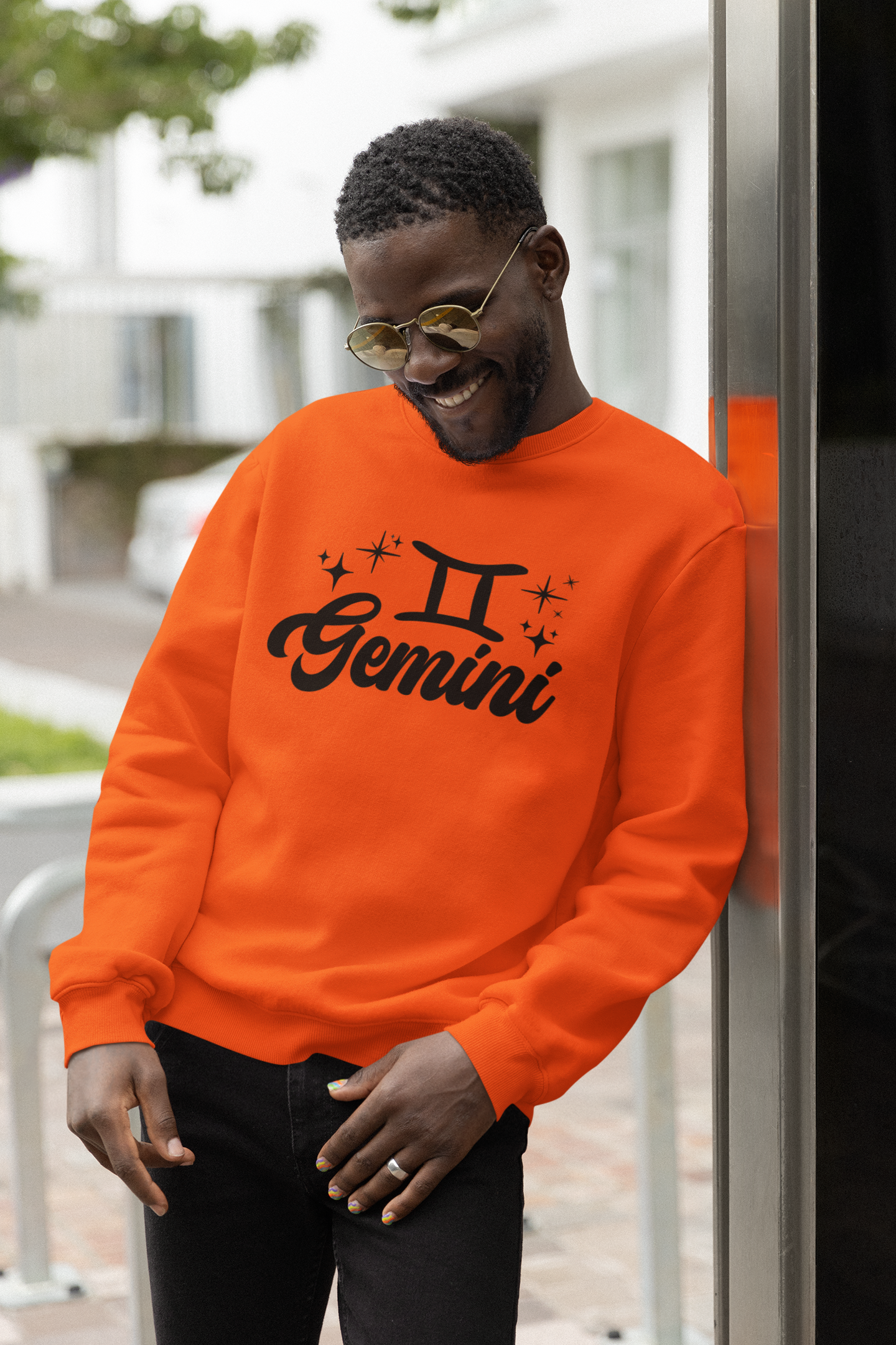 Person wearing a orange 'Gemini' black text design sweatshirt with zodiac symbol outdoors.