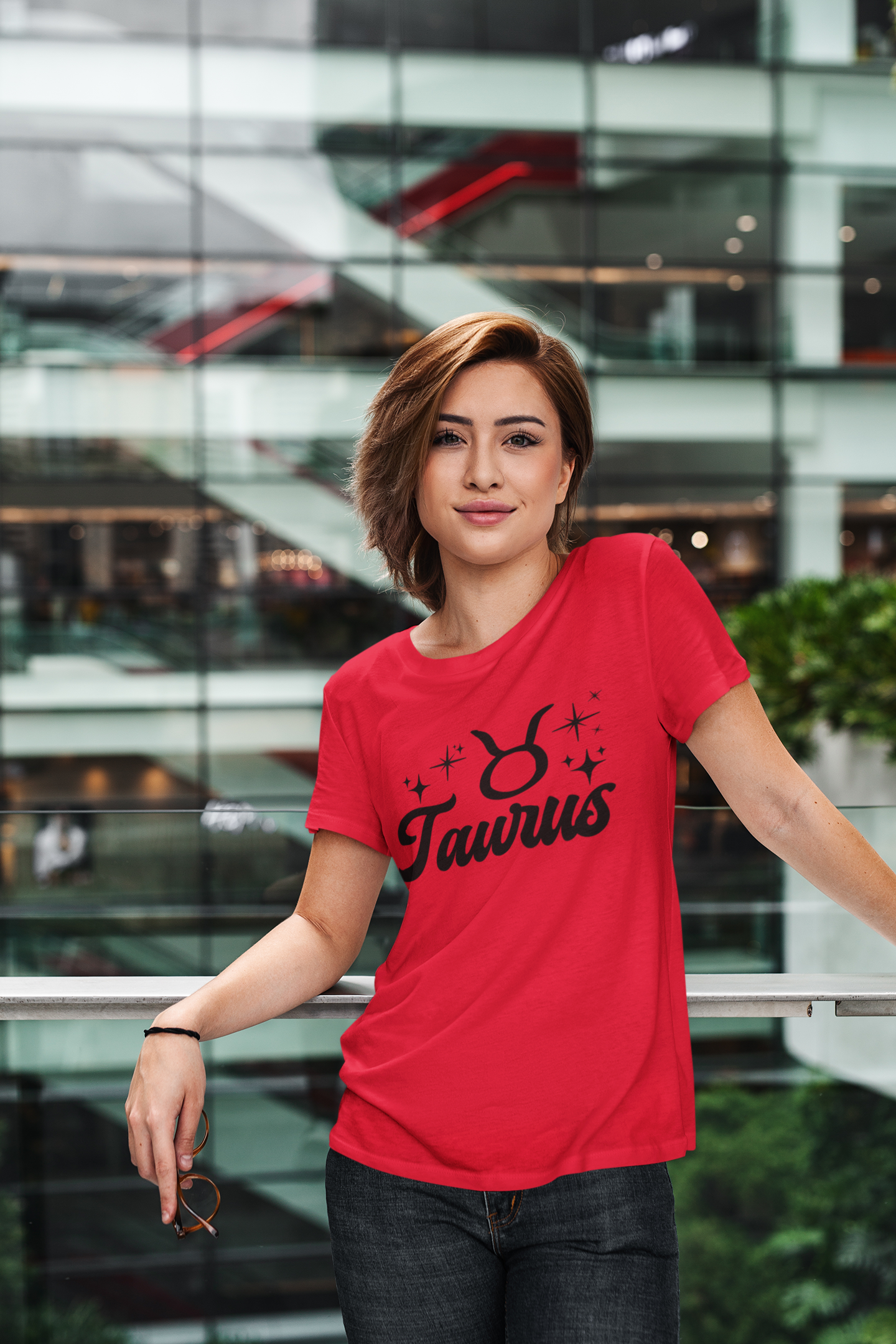 Person wearing a red Taurus t-shirt, black text design in front of a modern building.