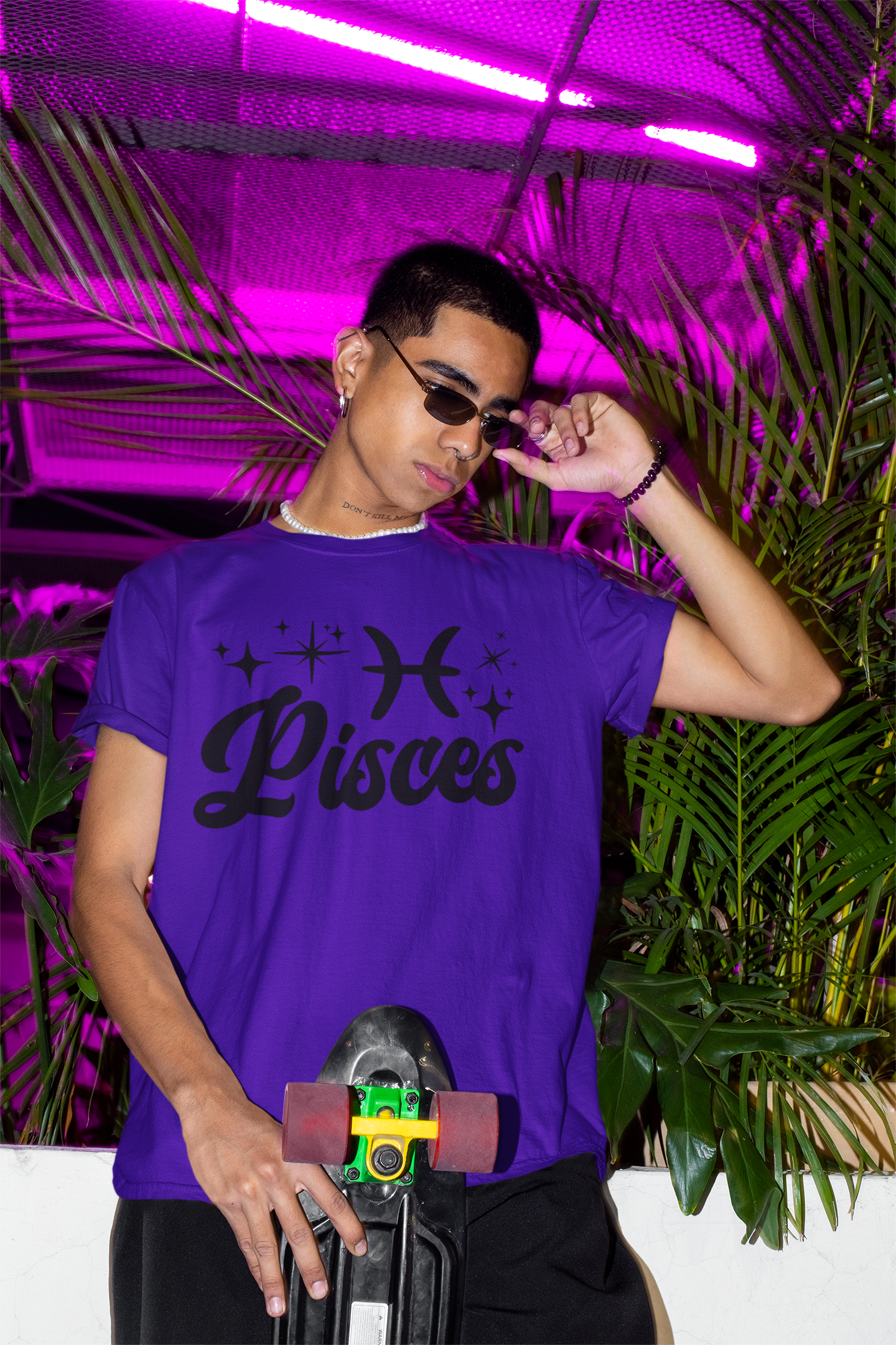 Person wearing a purple with black text 'Pisces' t-shirt holding a skateboard with a neon pink background