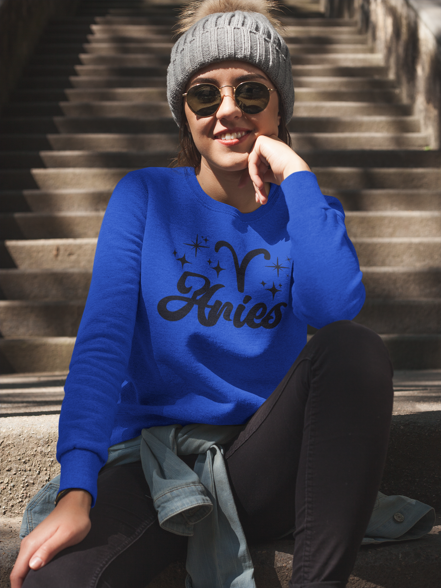 Person wearing a blue 'Aries' black text design sweatshirt sitting on steps.