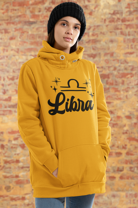 Person wearing a gold hoodie with 'Libra' black text design standing in front of a brick wall.