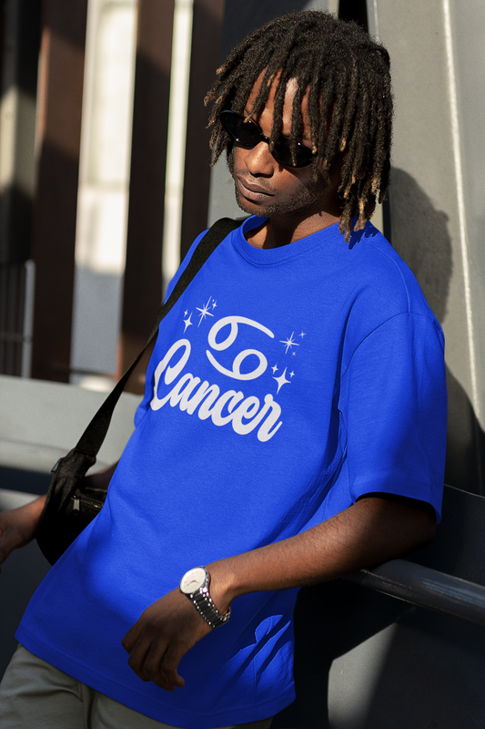 Person wearing a blue t-shirt with 'Cancer' white text design, standing against a building.