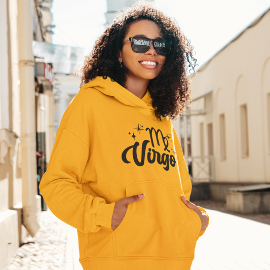 Woman with sunglasses, wearing a gold hoodie with "Virgo' black text design standing on the street.