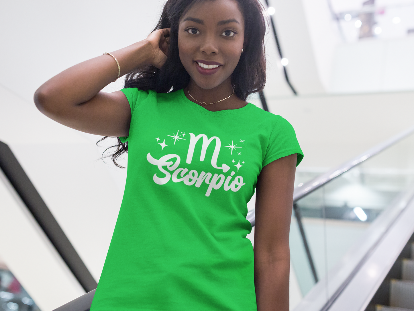 Woman wearing a green t-shirt with 'Scorpio' white text design, standing on escalator.