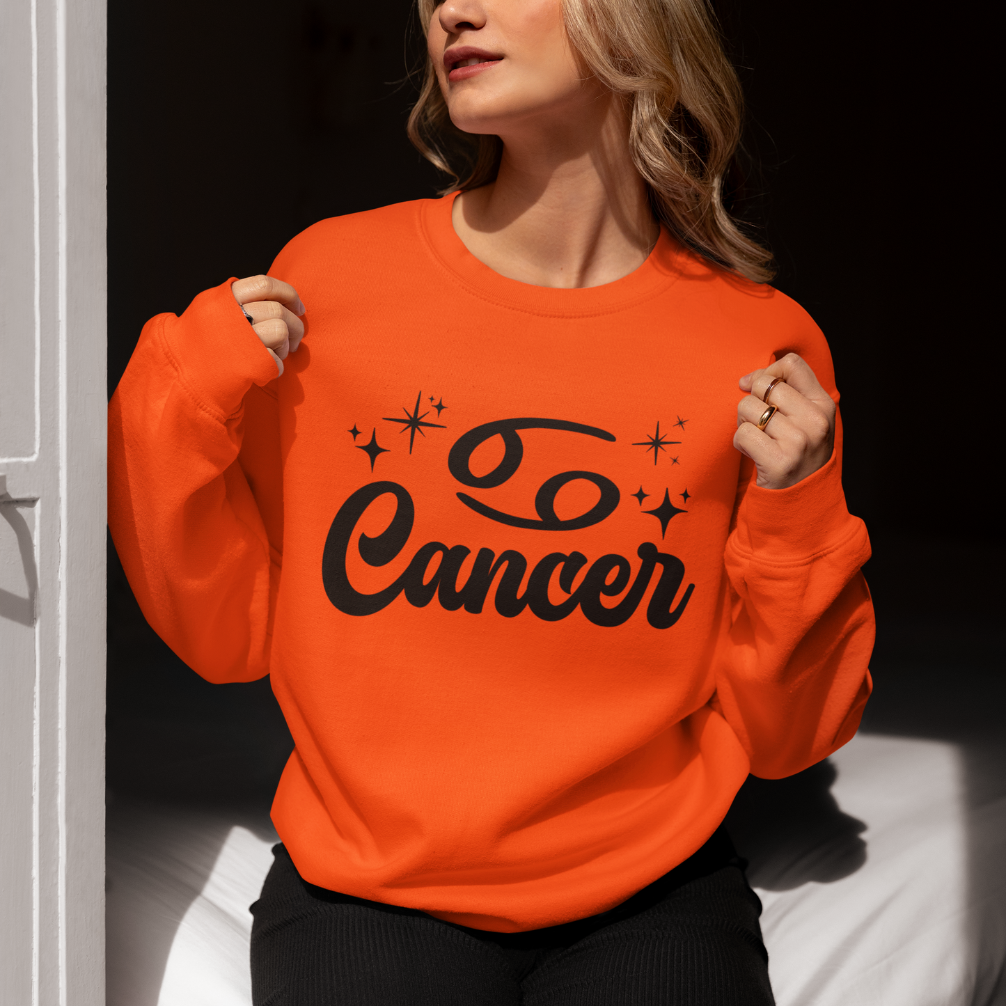 Person wearing a red sweatshirt with 'Cancer' black text, sitting indoors.