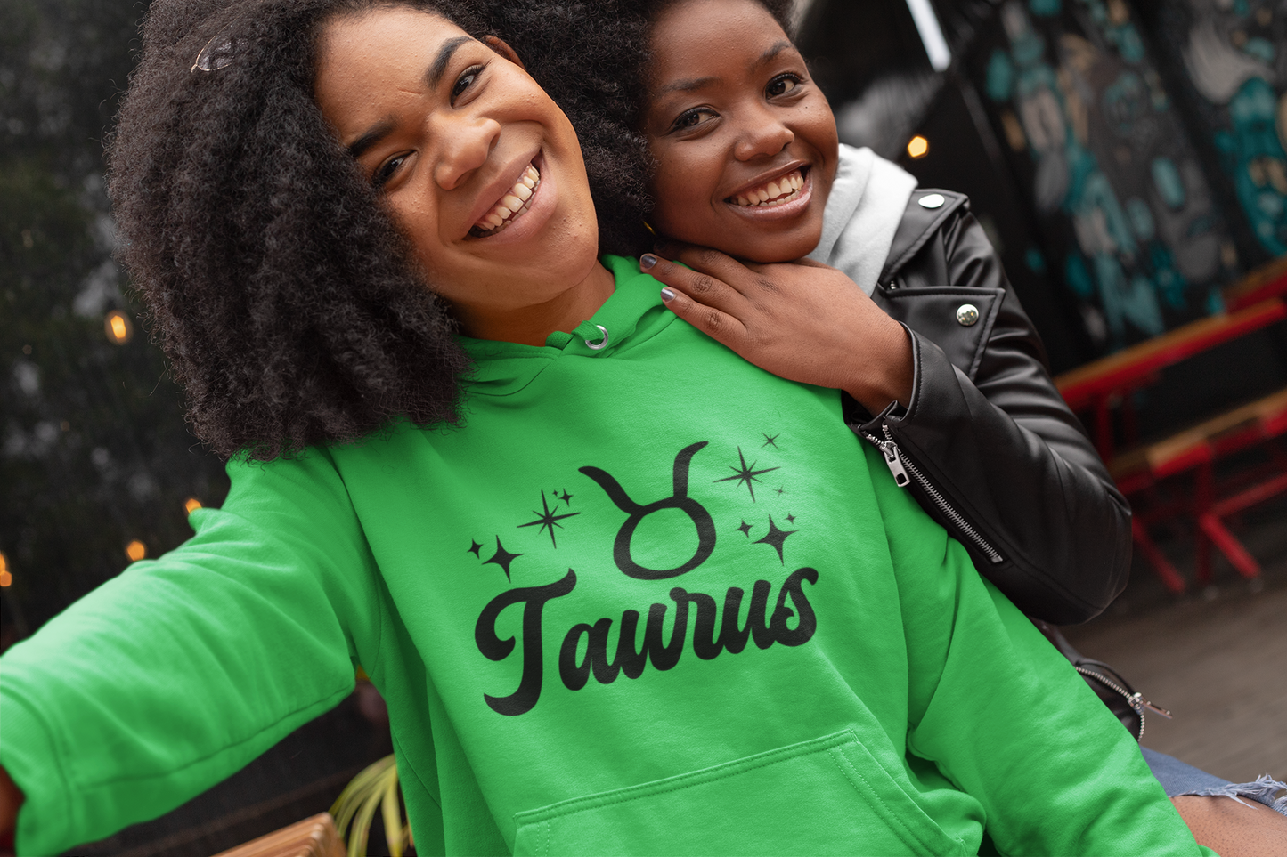 Two people posing together, one wearing a green 'Taurus' hoodie, black text design 