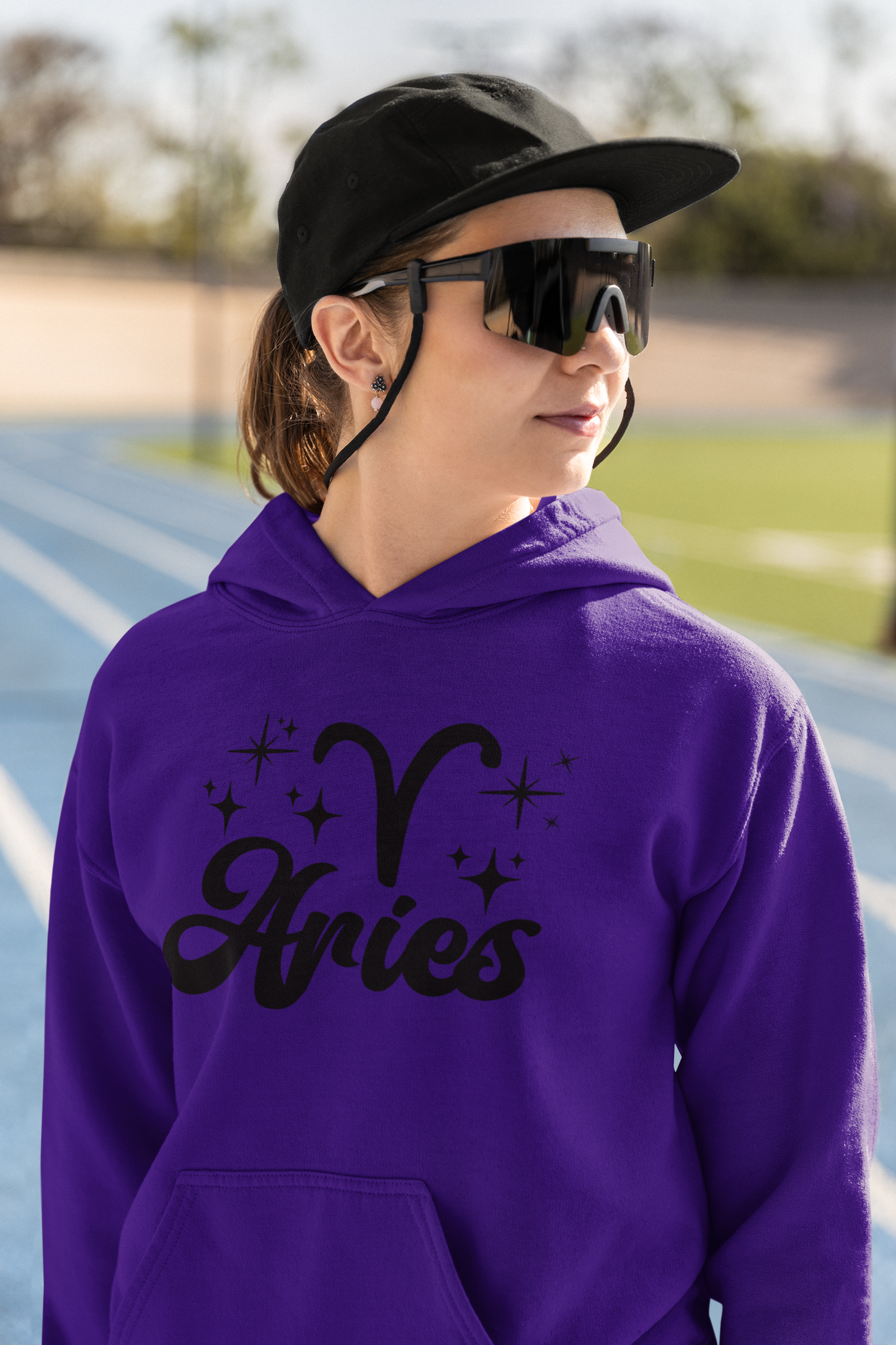 Person wearing a purple hoodie with black 'Aries' text and zodiac symbol outdoors.