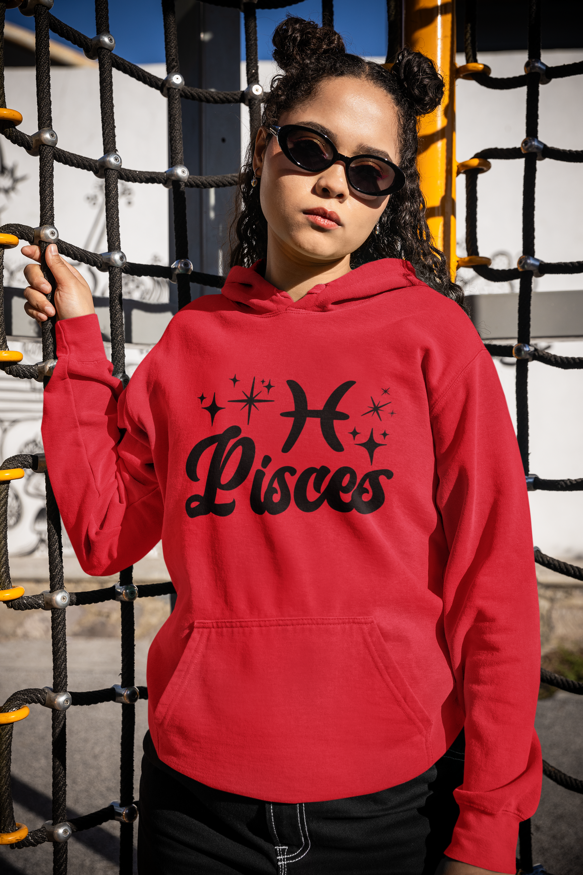 Person wearing a red hoodie with 'Pisces' black text with zodiac symbol, standing in front of playground equipment.