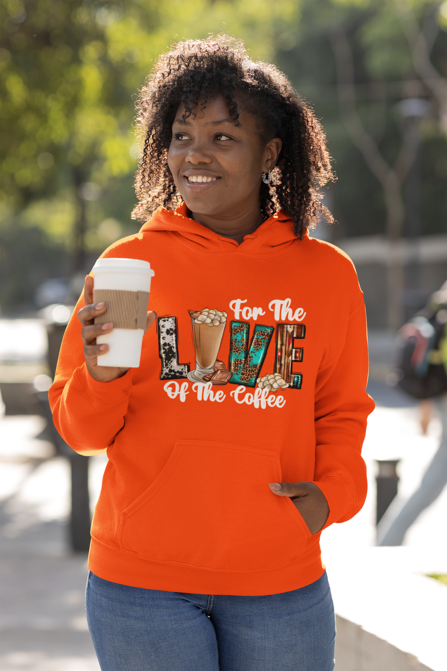Person wearing a cozy coffee orange hoodie with a coffee-themed design, holding a coffee cup outdoors.