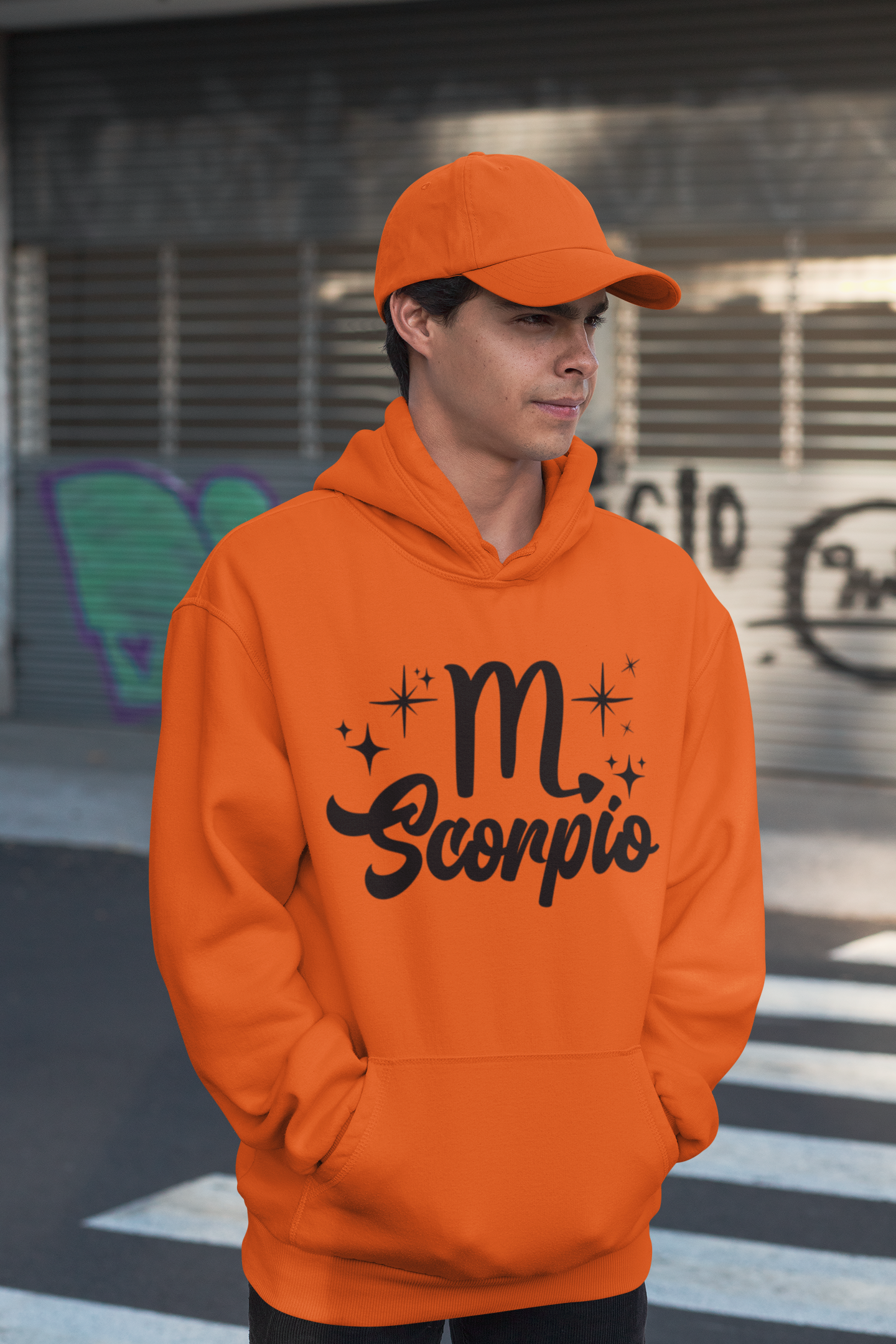 Person wearing a orange hoodie with 'Scorpio' black text design, standing on a street.