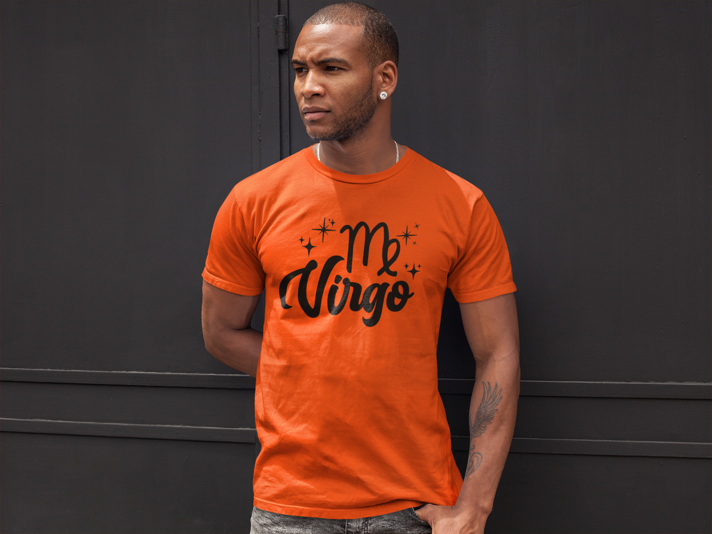 Man wearing a orange t-shirt with 'Virgo' black text against a black wall background