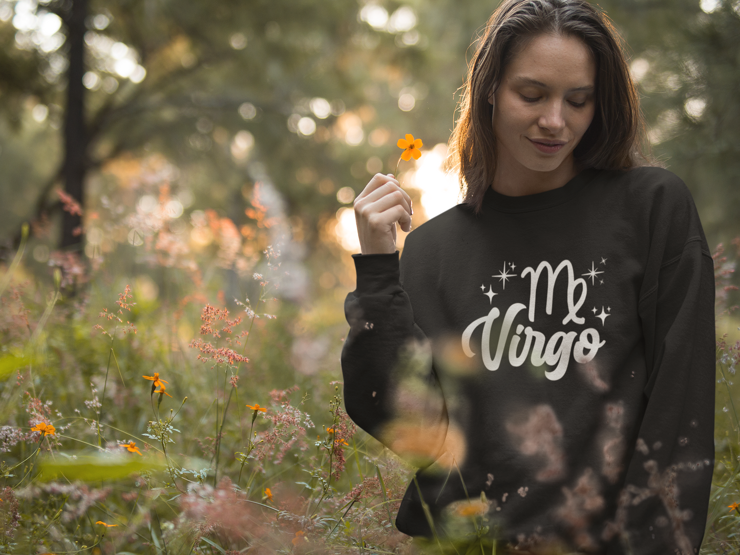 Woman wearing a black 'Virgo' white text design sweatshirt in a field of flowers