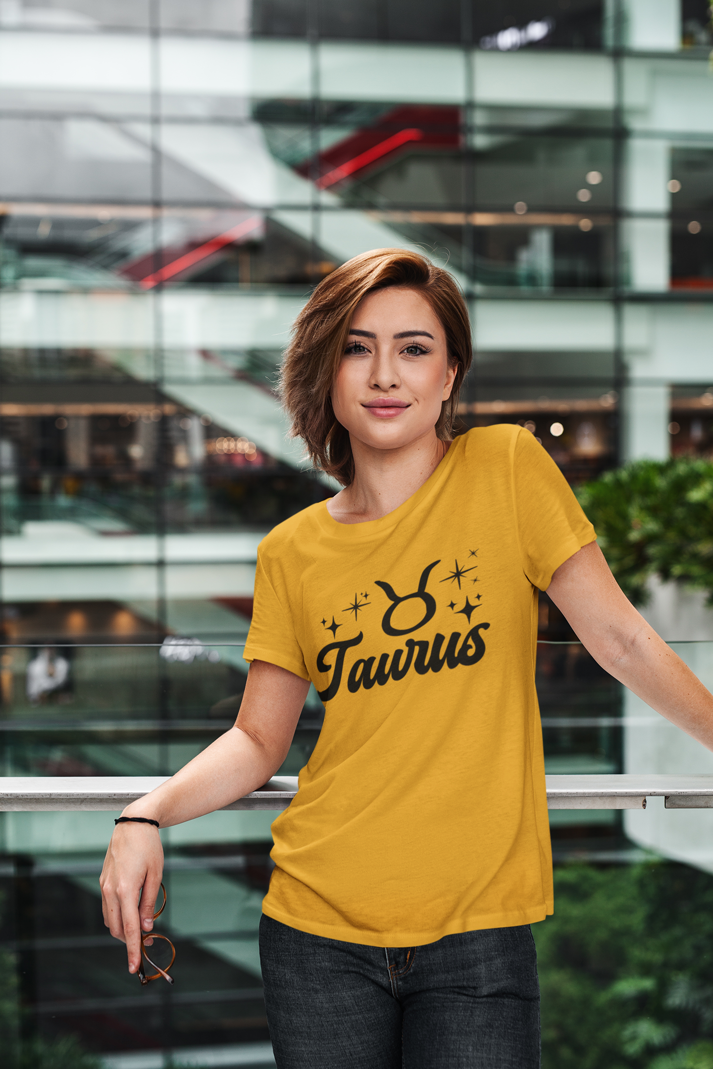 Person wearing a gold Taurus t-shirt, black text design in front of a modern building.
