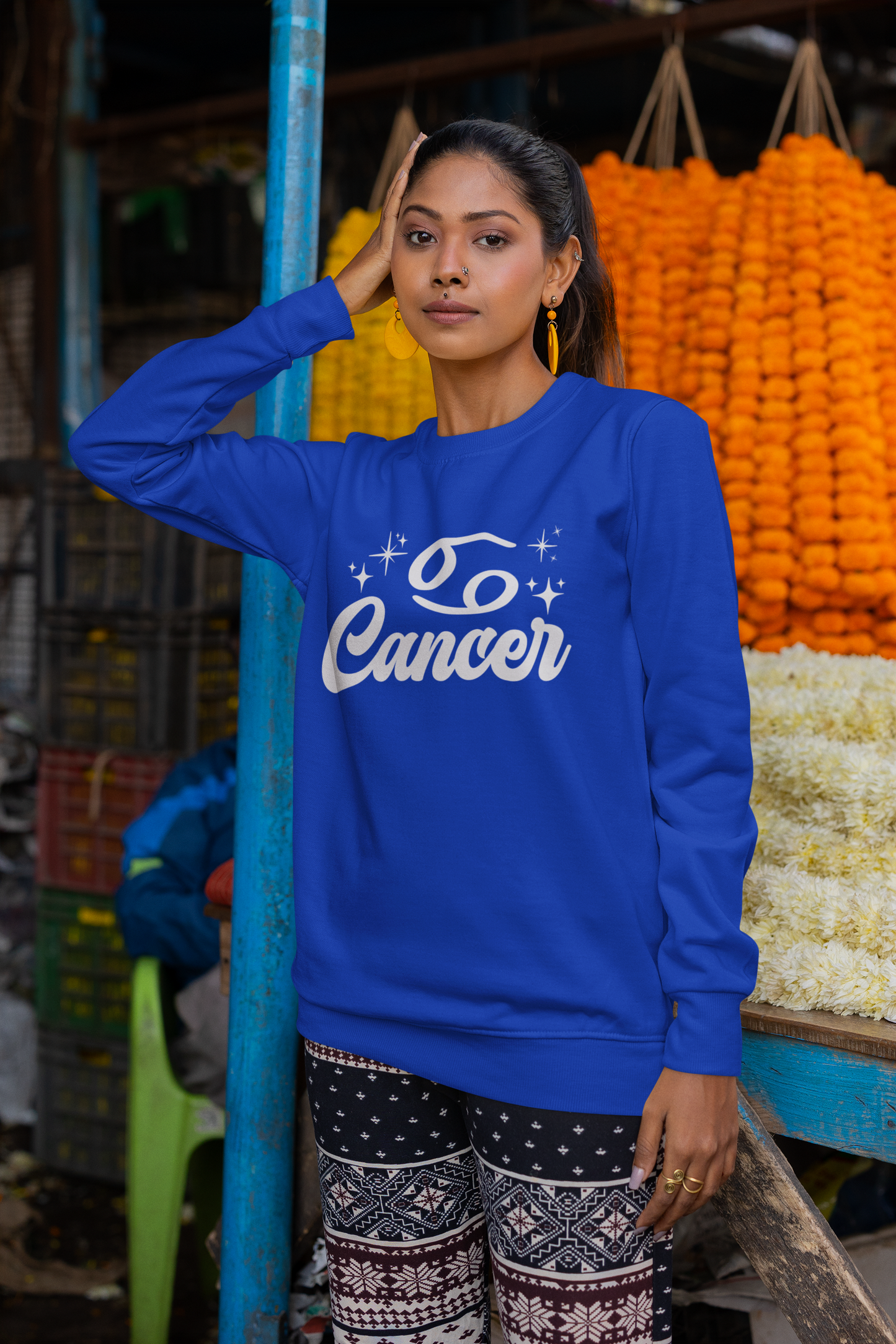 Woman wearing a blue sweatshirt with 'Cancer' white text in an outdoor market setting