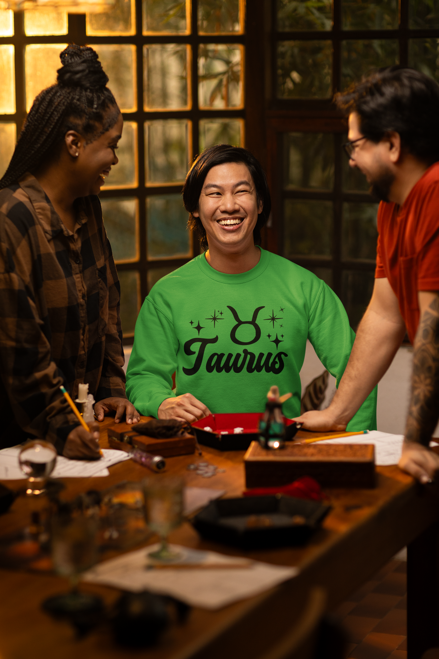 Three people around a table with a focus on a person wearing a green 'Taurus' black text t-shirt.