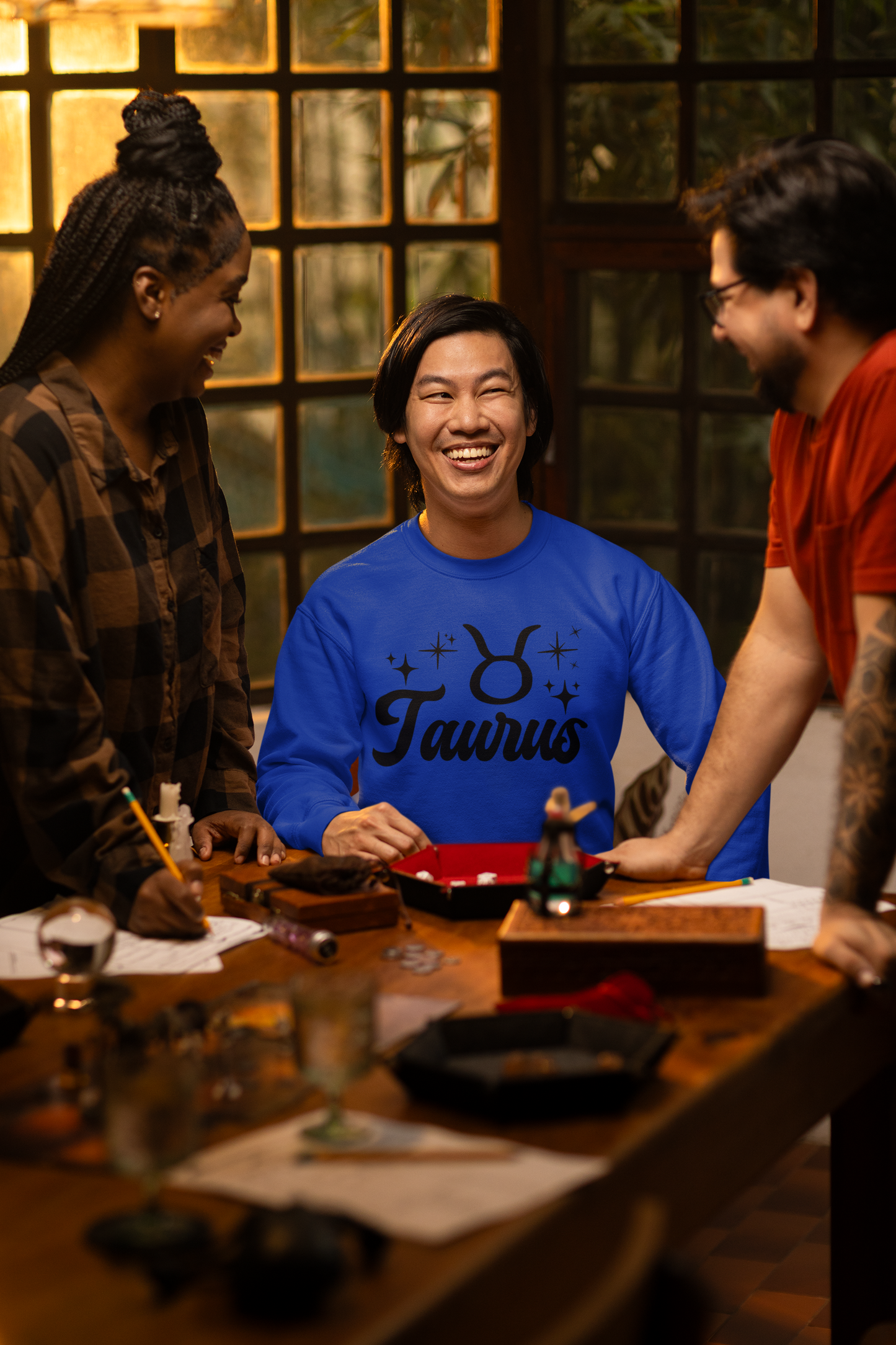 Three people around a table with a focus on a person wearing a blue 'Taurus' black text t-shirt.