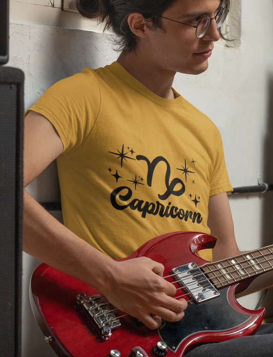 Person wearing a gold t-shirt with 'Capricorn' black text design holding a red guitar.