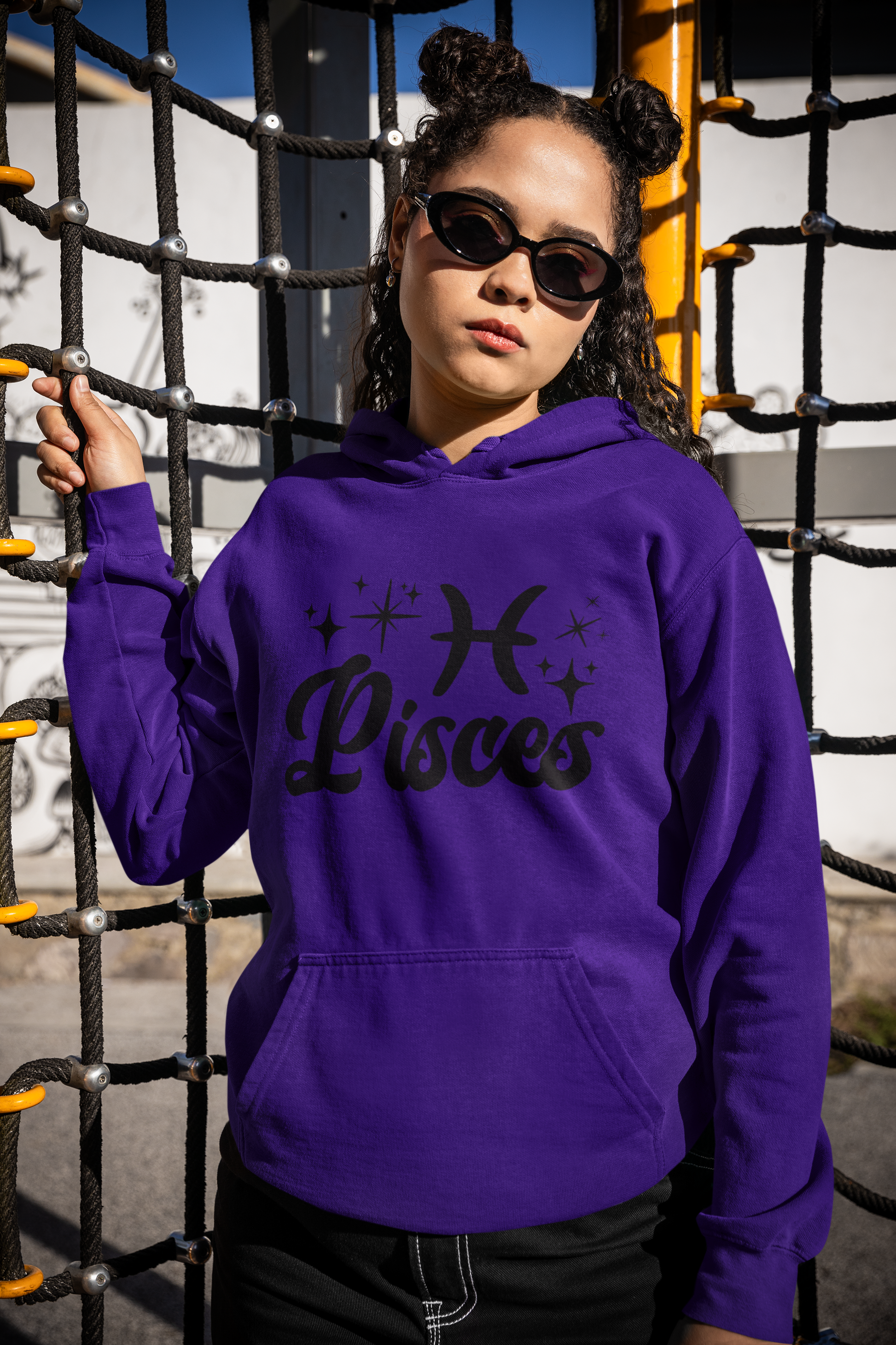 Person wearing a purple hoodie with 'Pisces' black text with zodiac symbol, standing in front of playground equipment.