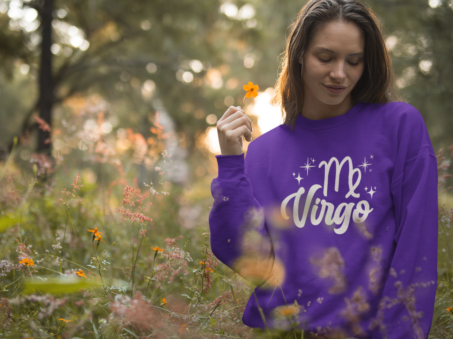 Woman wearing a purple 'Virgo' white text design sweatshirt in a field of flowers