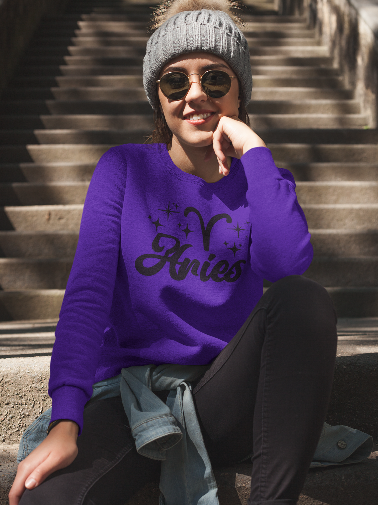 Person wearing a purple 'Aries' black text design sweatshirt sitting on steps.