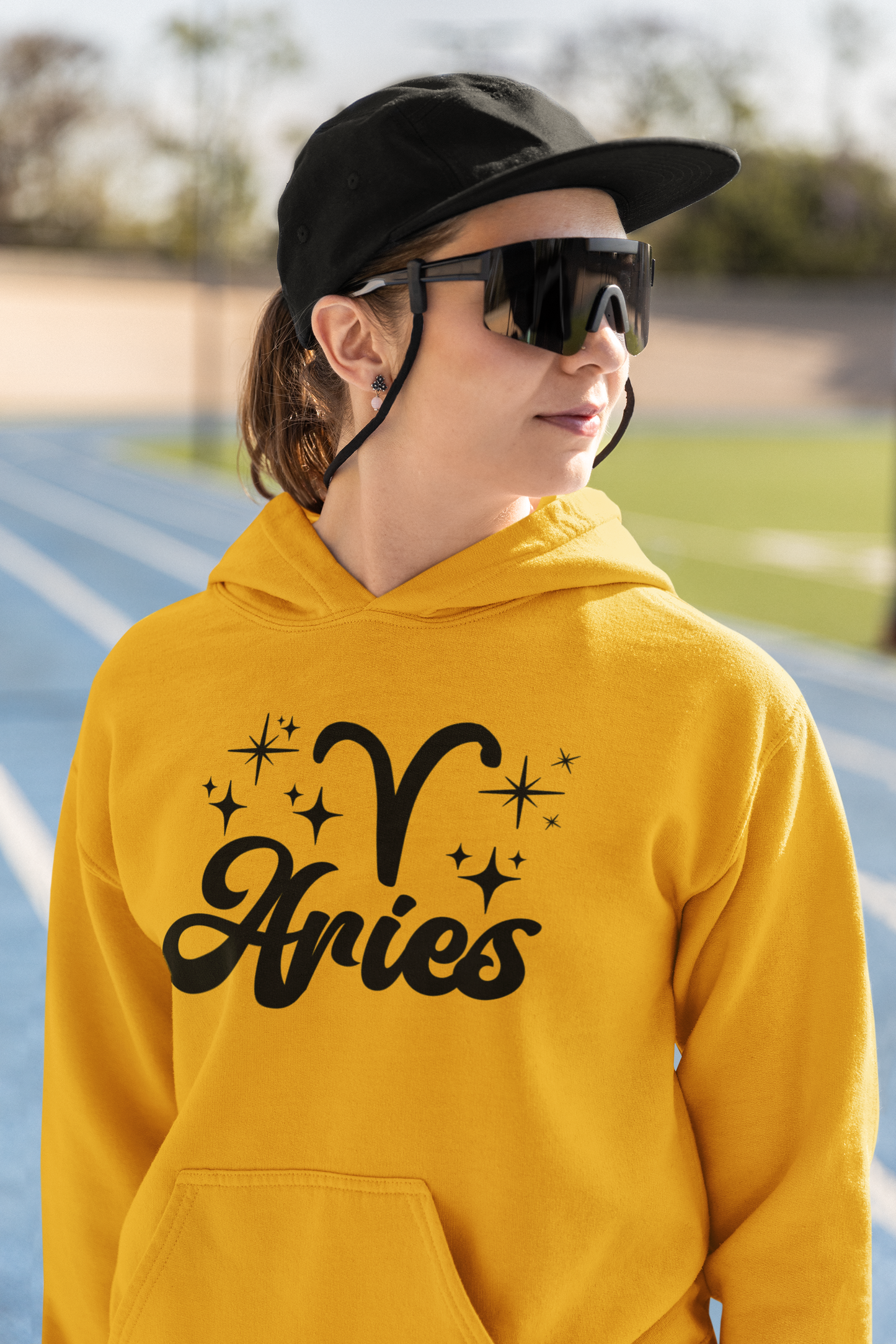 Person wearing a gold hoodie with black 'Aries' text and zodiac symbol outdoors.