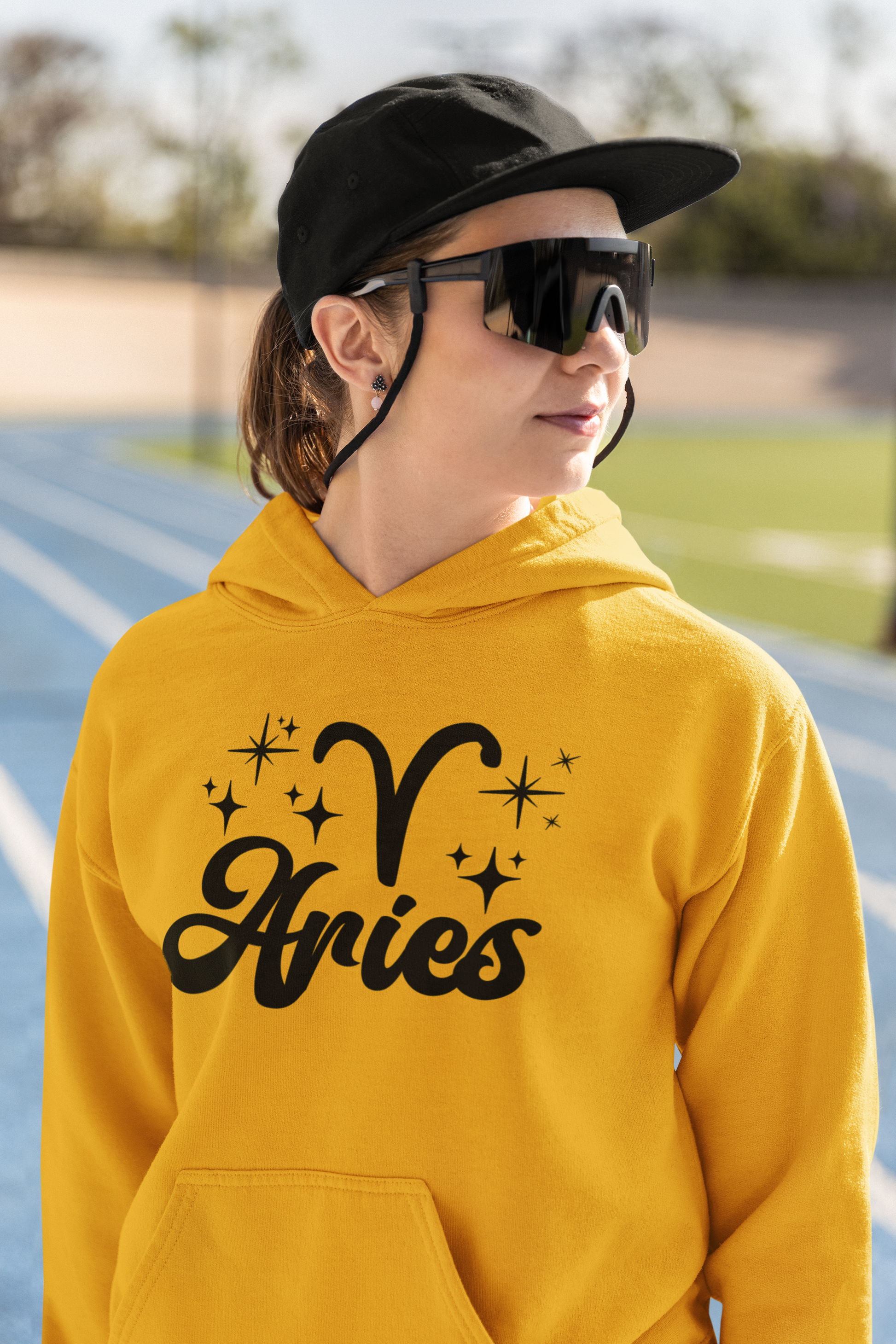 Person wearing a gold hoodie with black 'Aries' text and zodiac symbol outdoors.