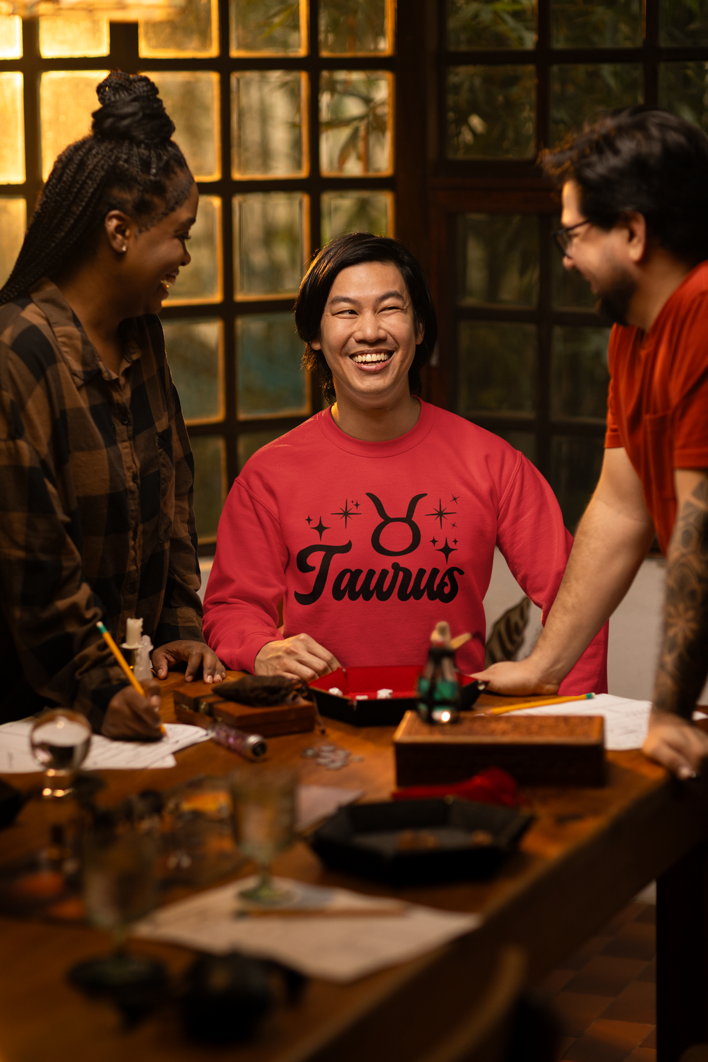 Three people around a table with a focus on a person wearing a red 'Taurus' black text t-shirt.