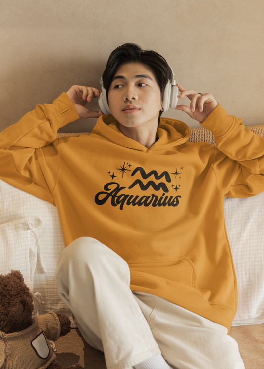 Person wearing a gold hoodie with 'Aquarius' black text with zodiac symbol, sitting on a couch.
