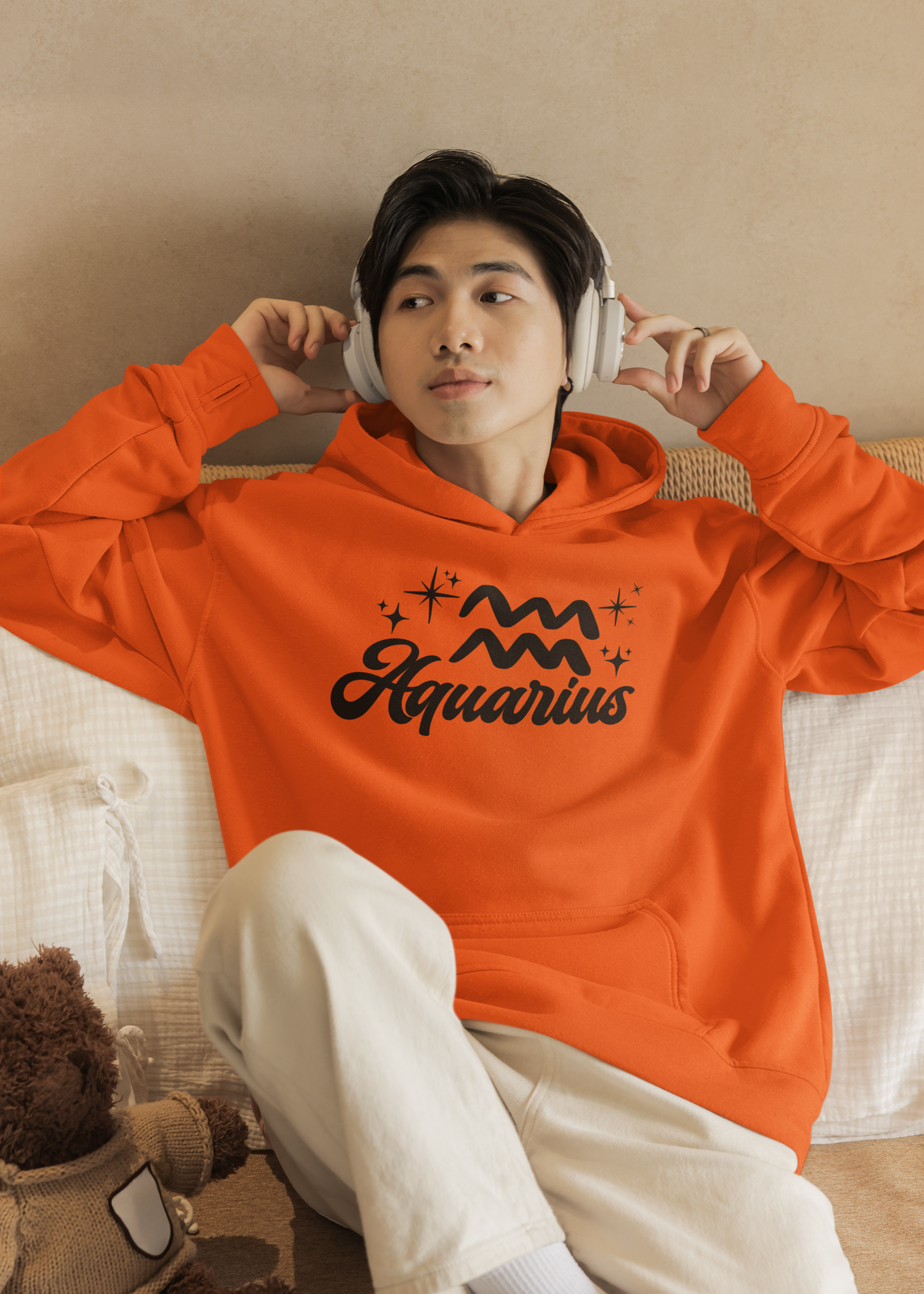 Person wearing a orange hoodie with 'Aquarius' black text with zodiac symbol, sitting on a couch.