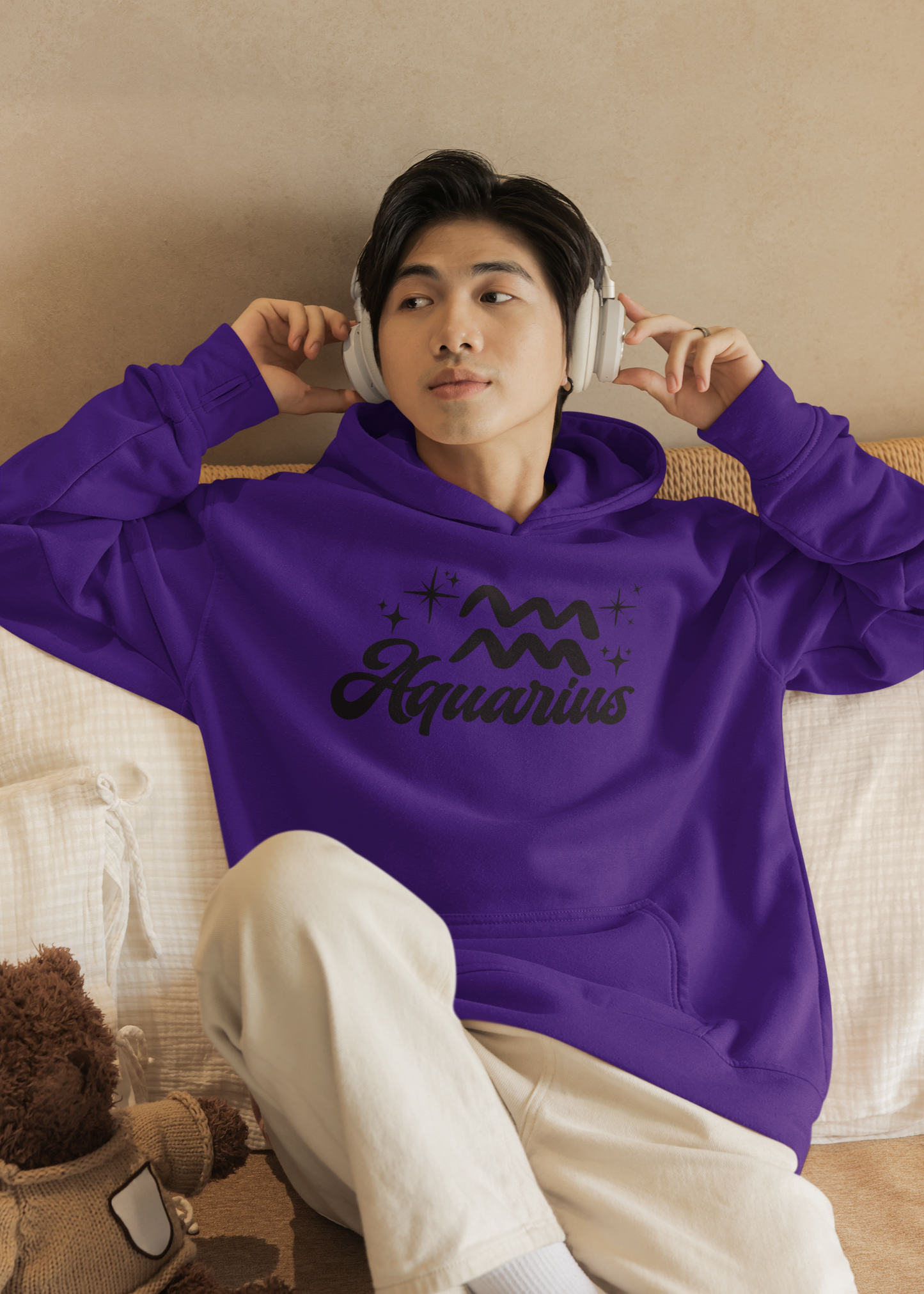 Person wearing a purple hoodie with 'Aquarius' black text with zodiac symbol, sitting on a couch.