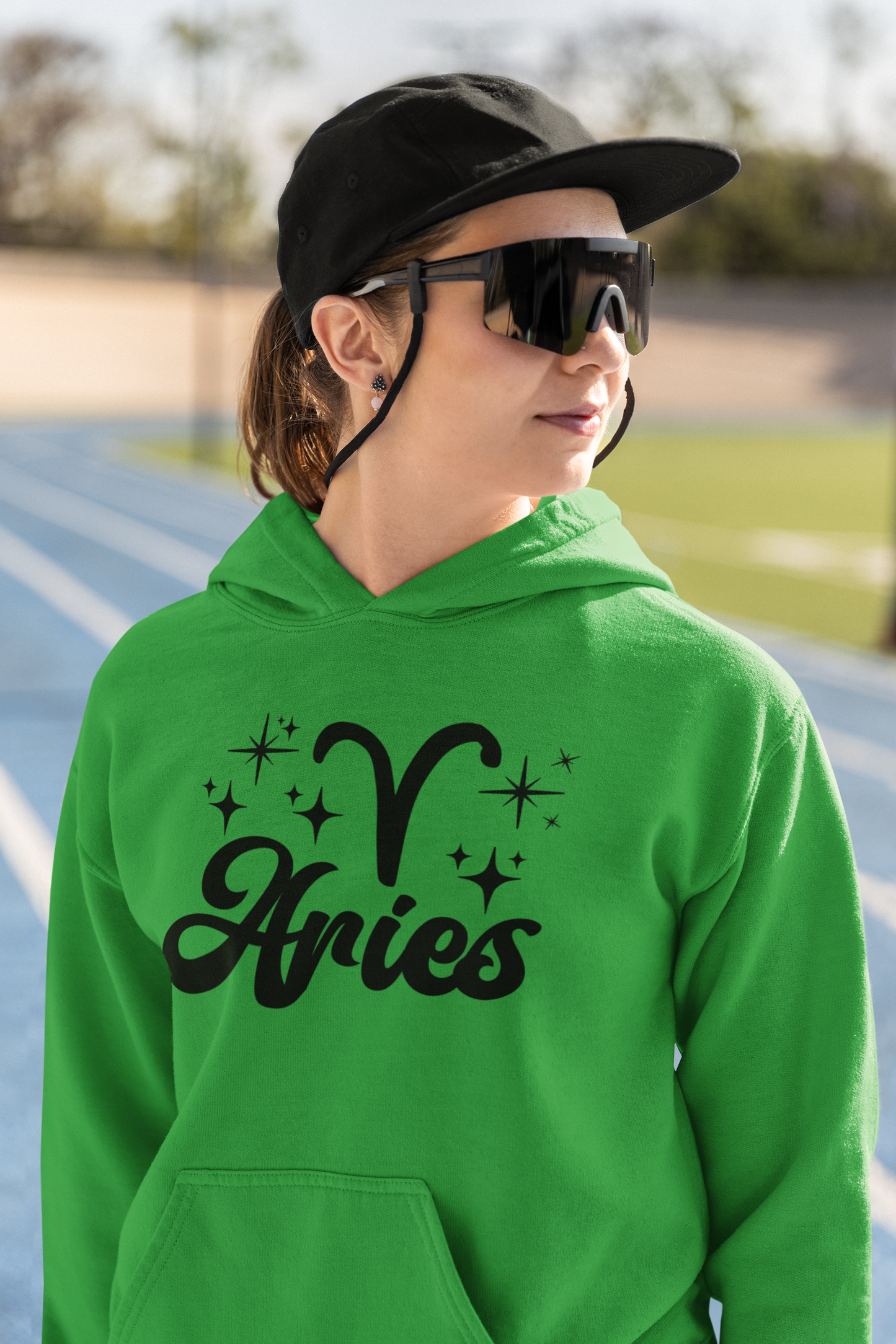 Person wearing a green hoodie with black 'Aries' text and zodiac symbol outdoors.