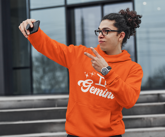 Person wearing an orange hoodie with 'Gemini' white text, taking a selfie outdoors.