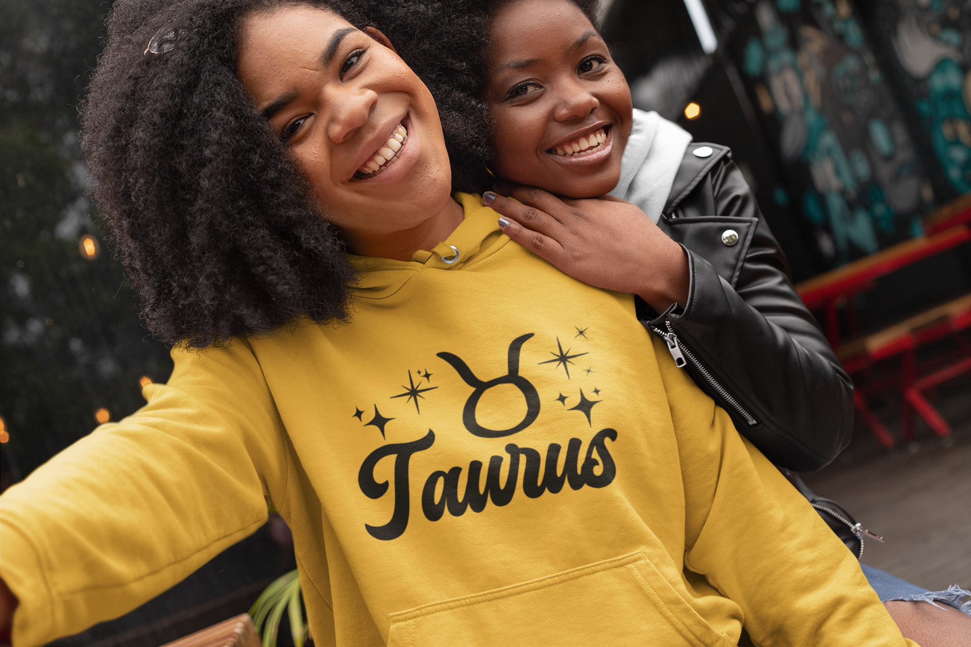Two people posing together, one wearing a gold 'Taurus' hoodie, black text design 